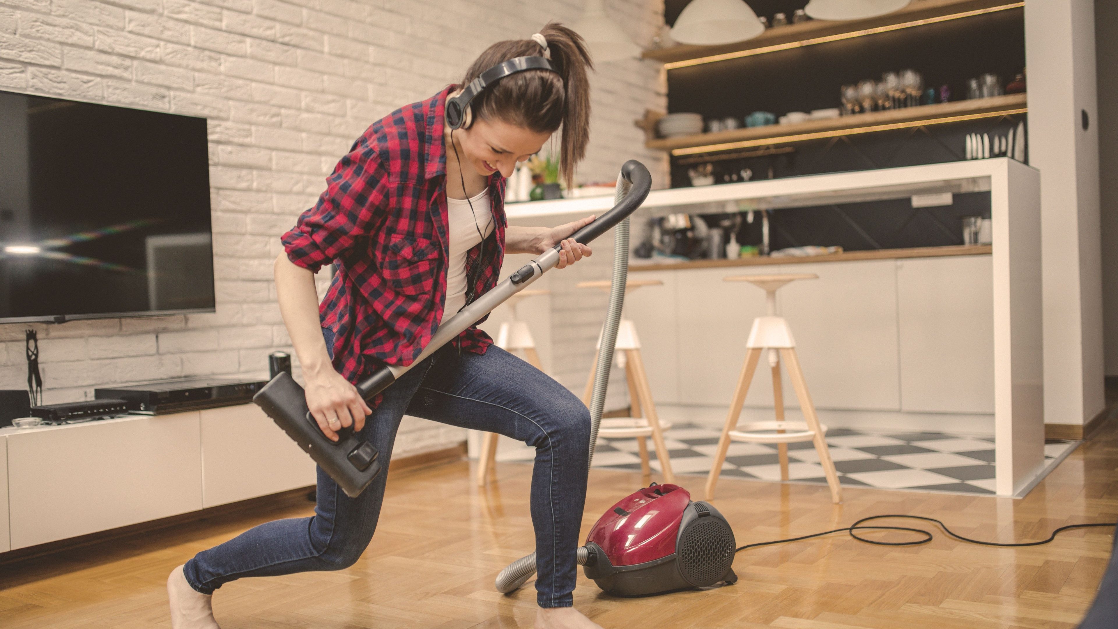 Young woman using vacuum cleaner to clean her house and listening music and playing imaginary guitar
