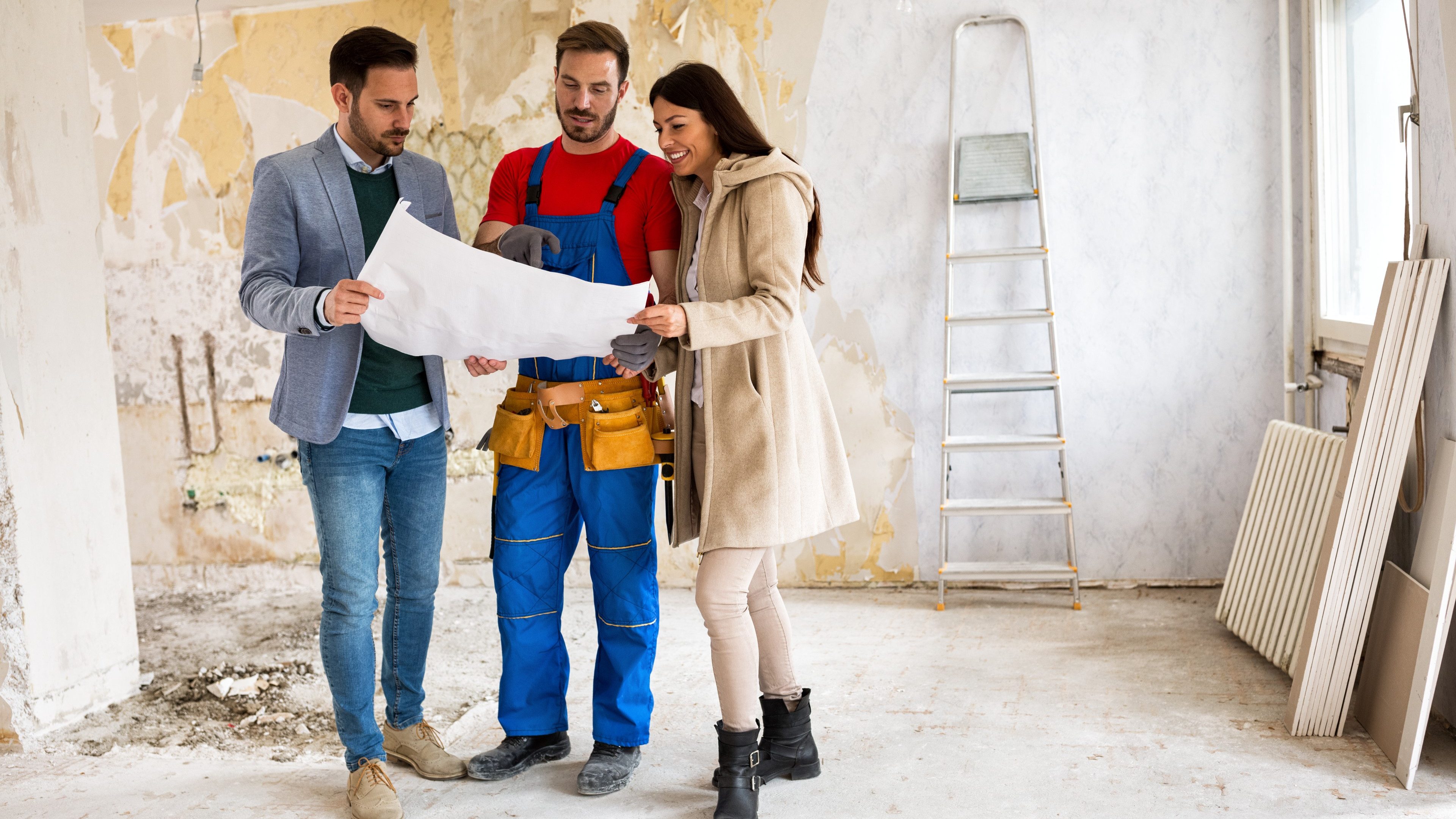 Beutiful young couple looking blueprints of their home with  builder handyman