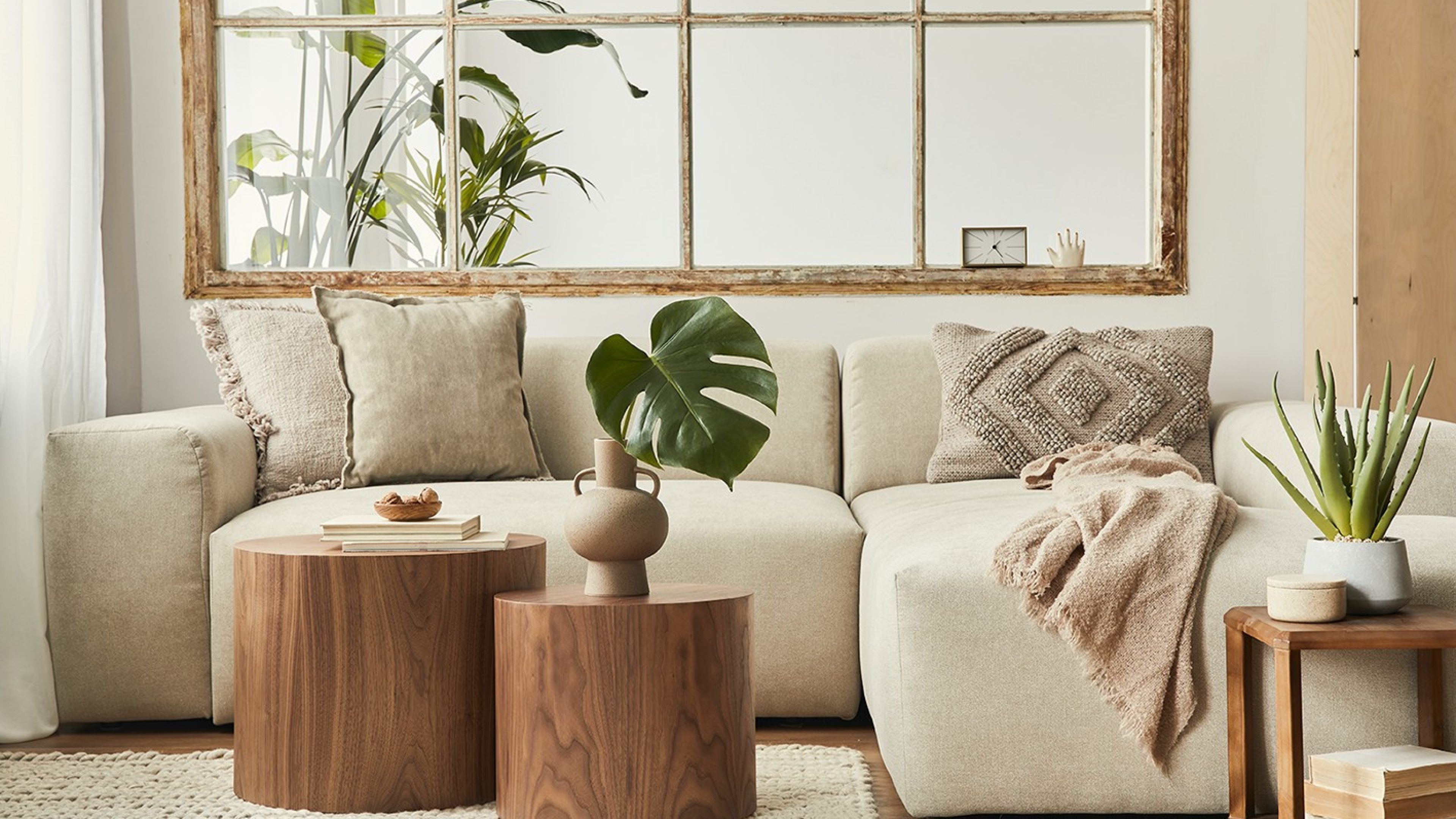 Interior design of living room with stylish modular beige sofa, wooden coffee tables, plants, pillows, plaid, neutral room divider, decoration and elegant accessories. Modern home decor. Template.