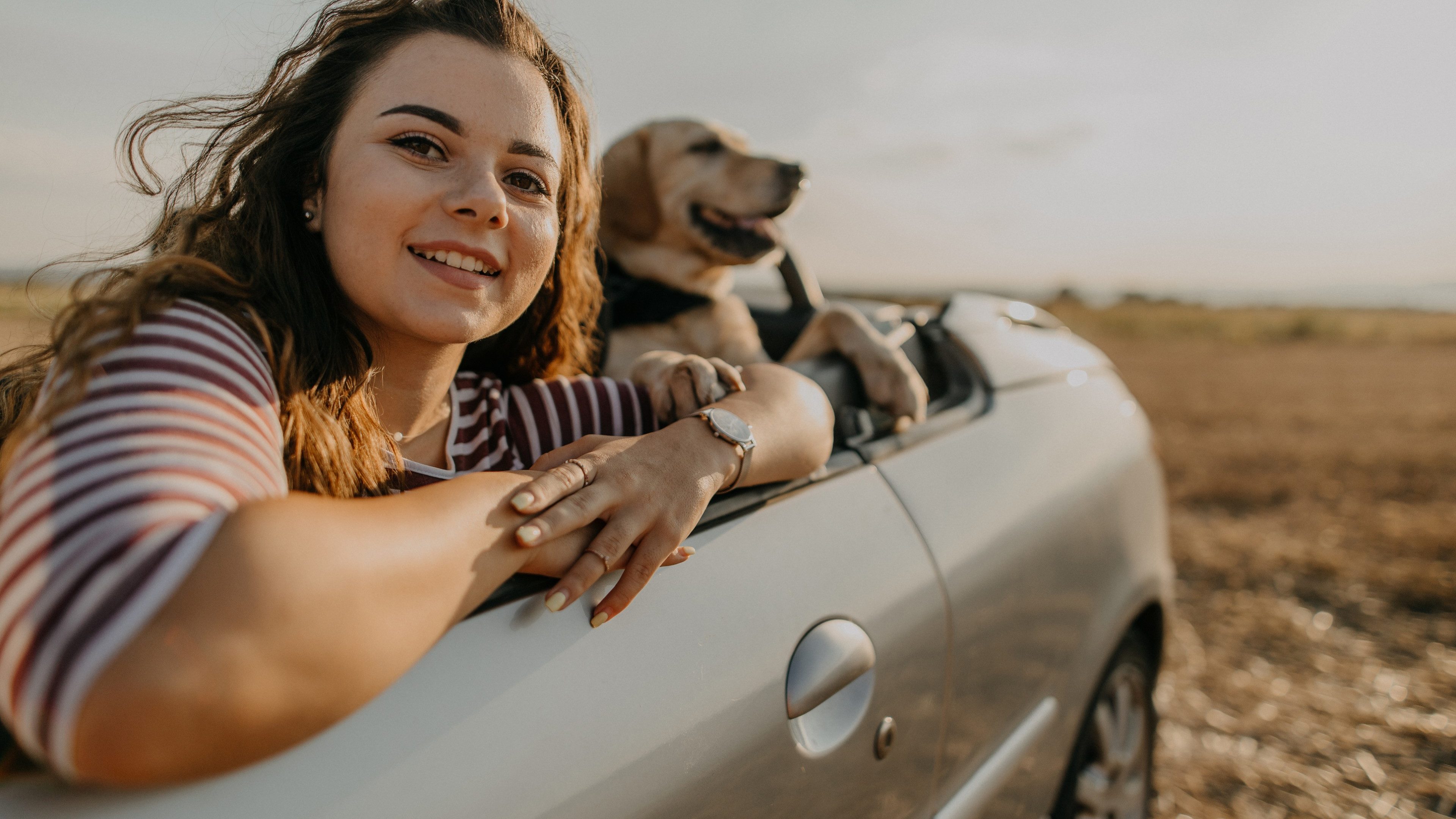 Girl with curly hair leaning on the door of her convertible with dog