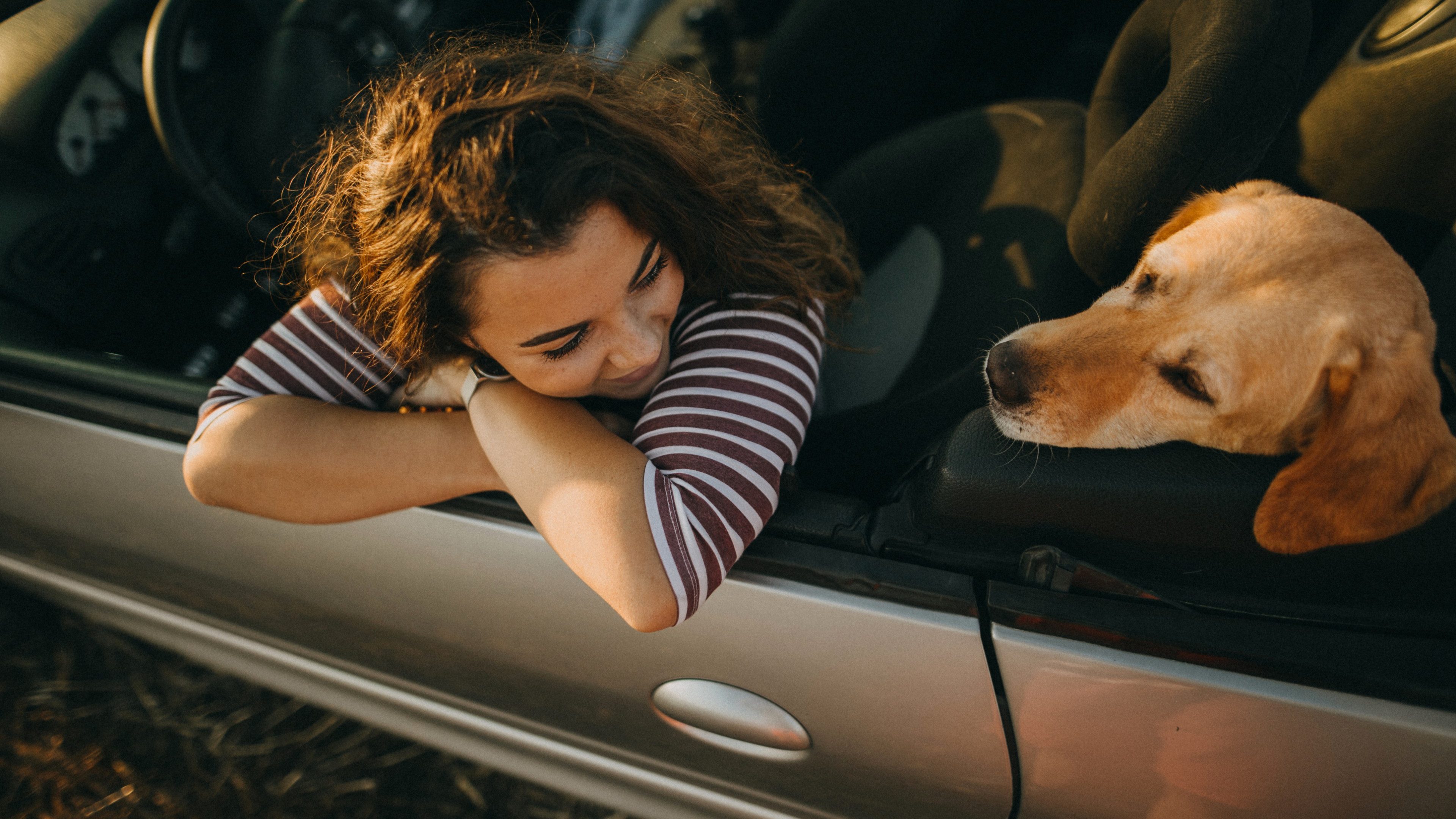 Girl with curly hair leaning on the door of her convertible with dog