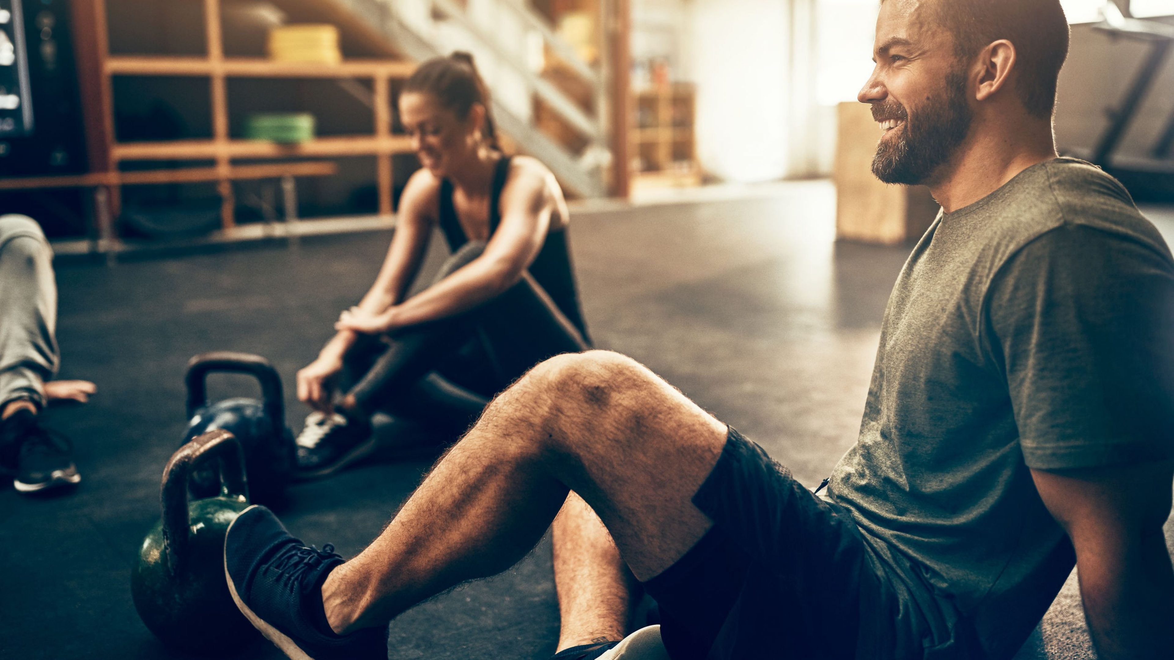 Fit people in exercise gear sitting on the floor of a gym laughing together after a workout