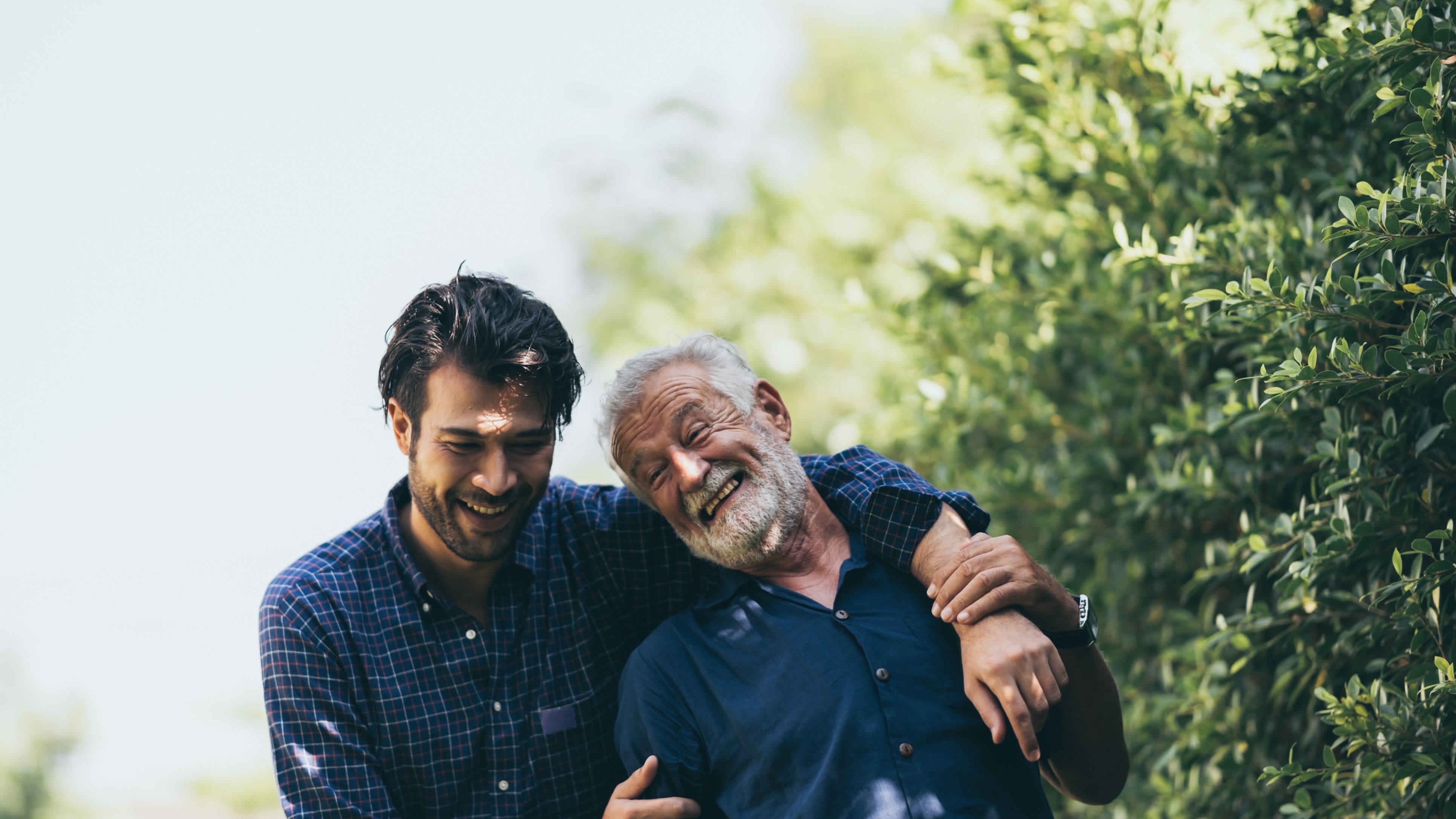 Vater und Sohn stehen vor Bäumen und umarmen sich lachend