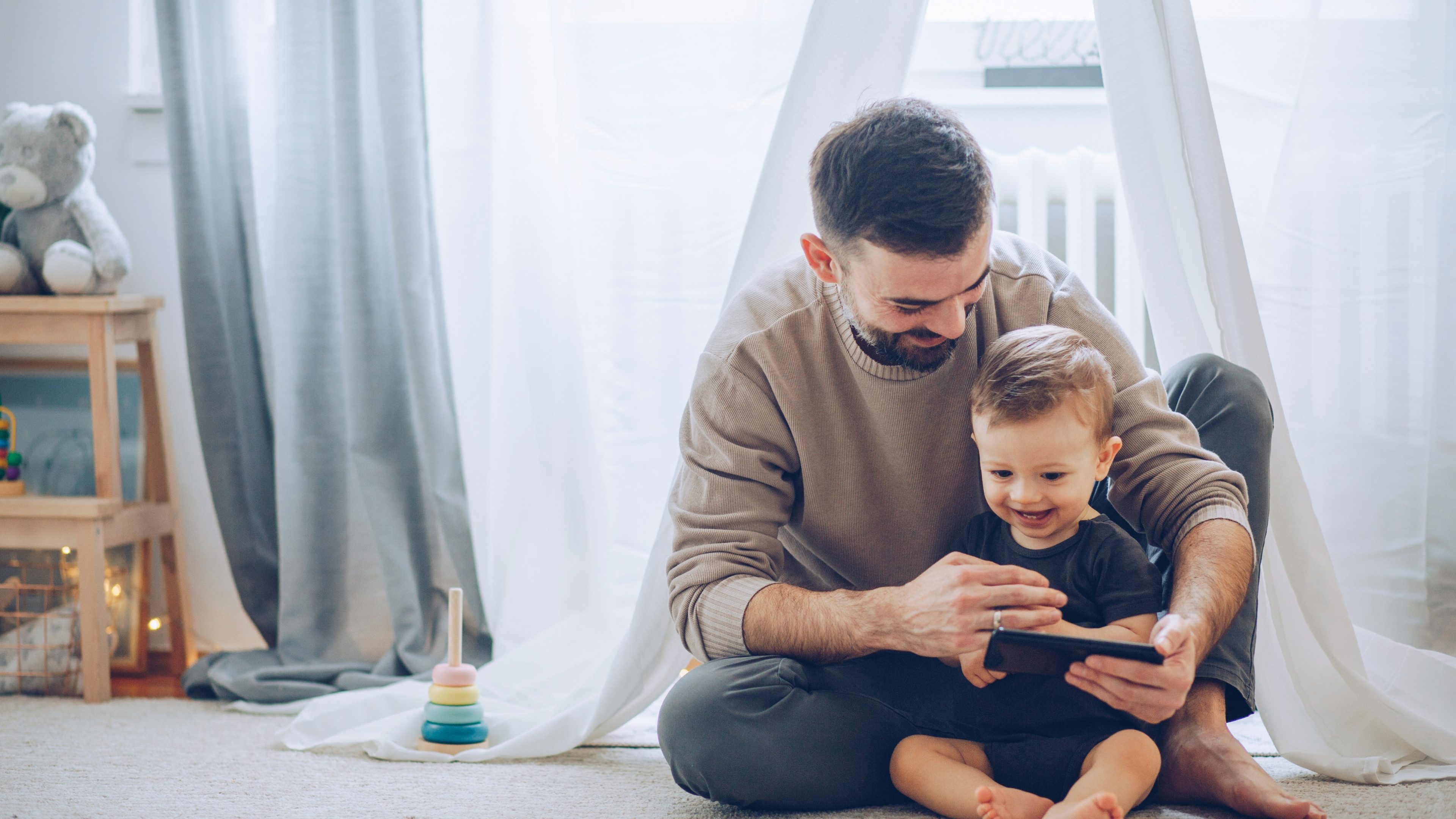 Father and son sitting on floor and watching favorite cartoon on mobile phone