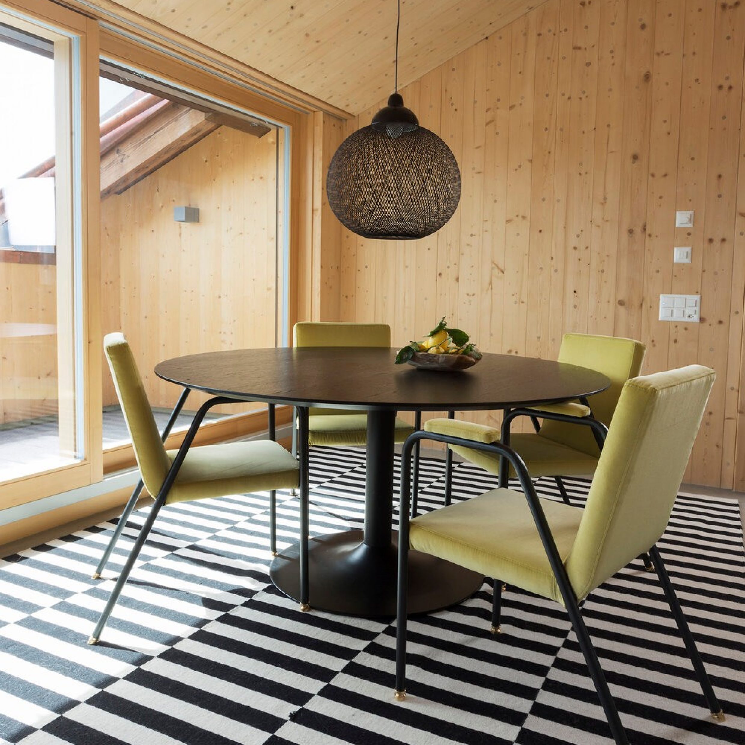 Ein Esszimmer mit einem runden Tisch und vier Stühlen, welche auf einem schwarzweiss gestreiften Teppich stehen.