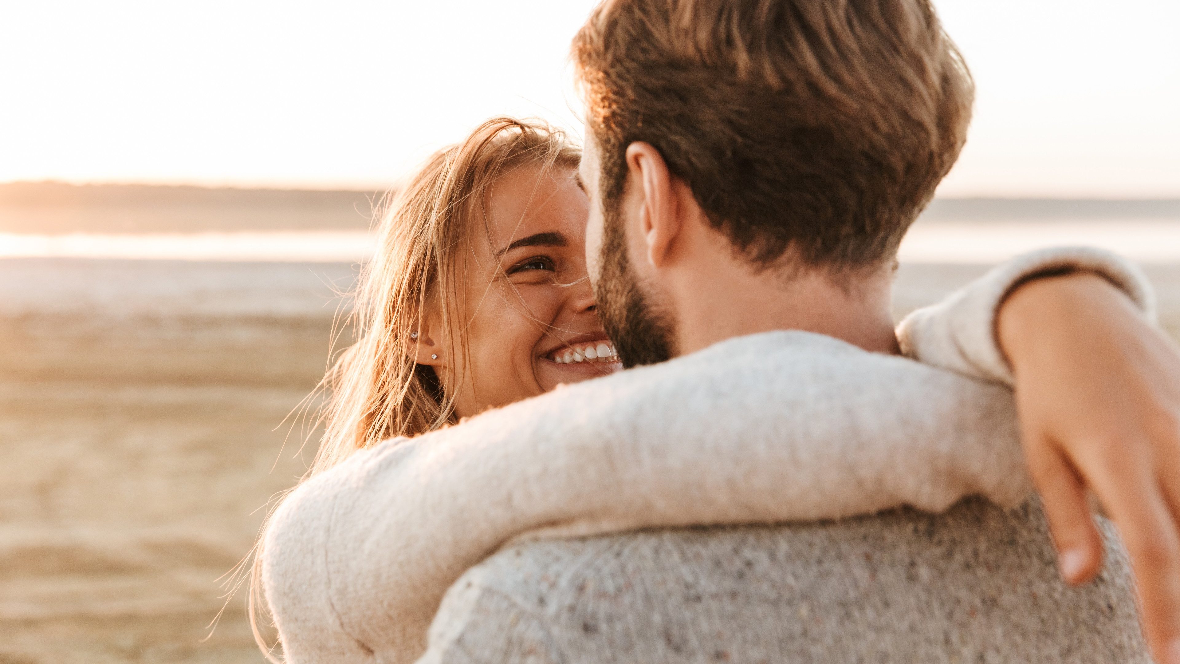 Close up back view of a beautiful smiling young couple standing at the sunny beach, embracing