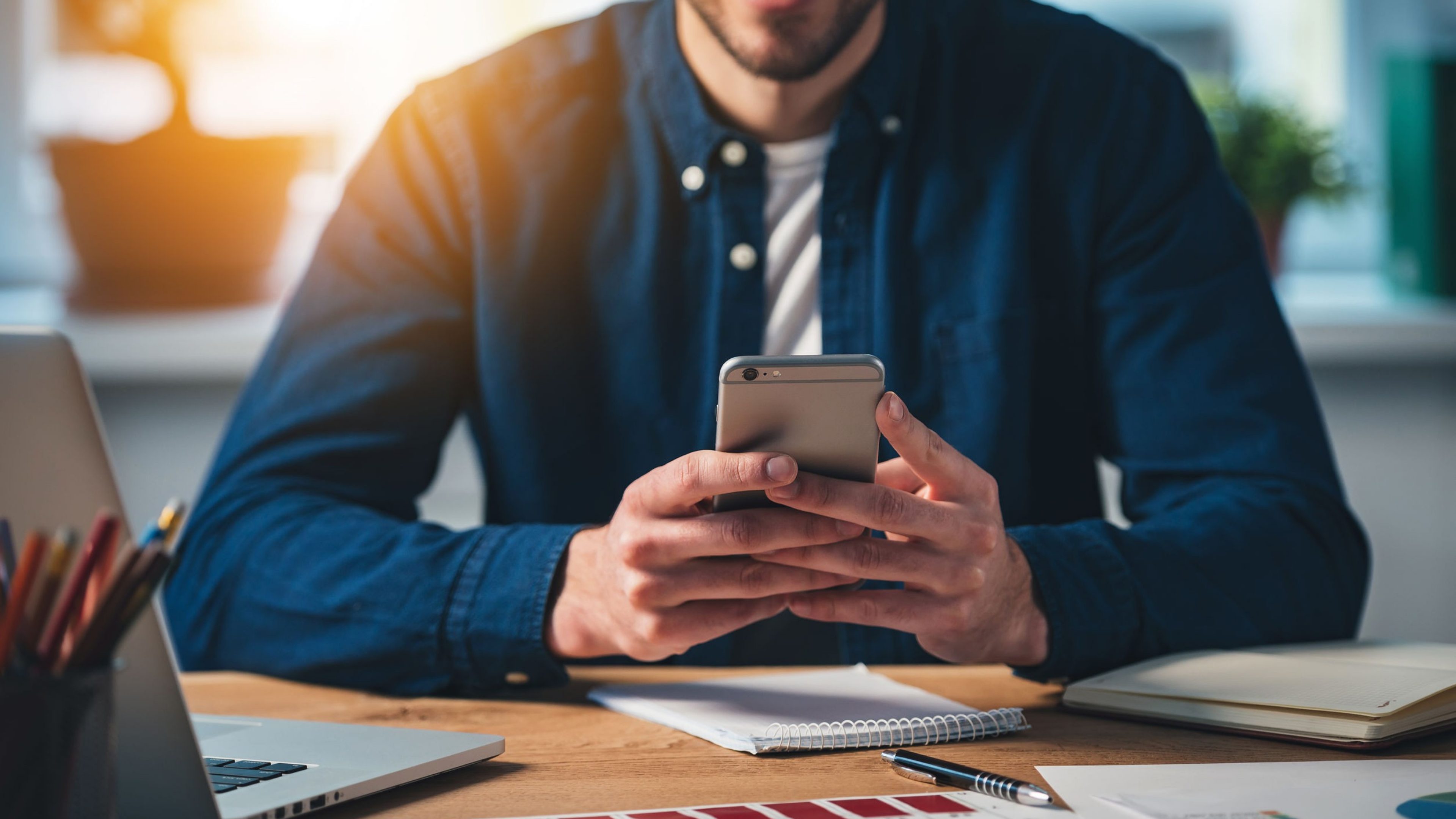 New message! Close-up part of cheerful young man using his smartphone with smile while sitting at his working place