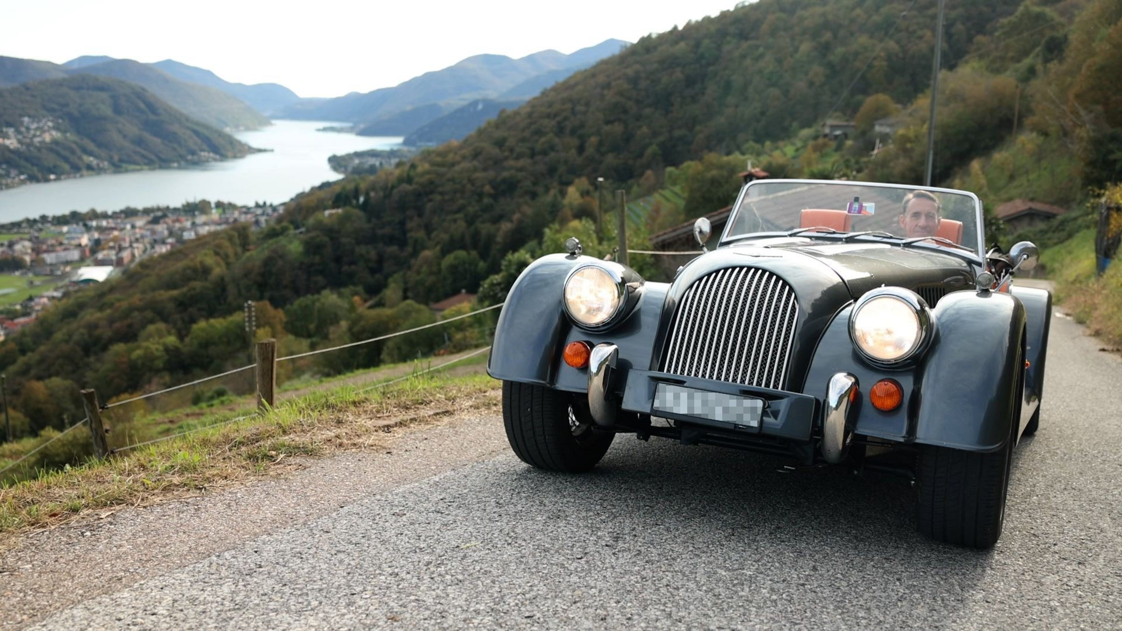 Ein Mann fährt im Oldtimer eine Strasse bergauf