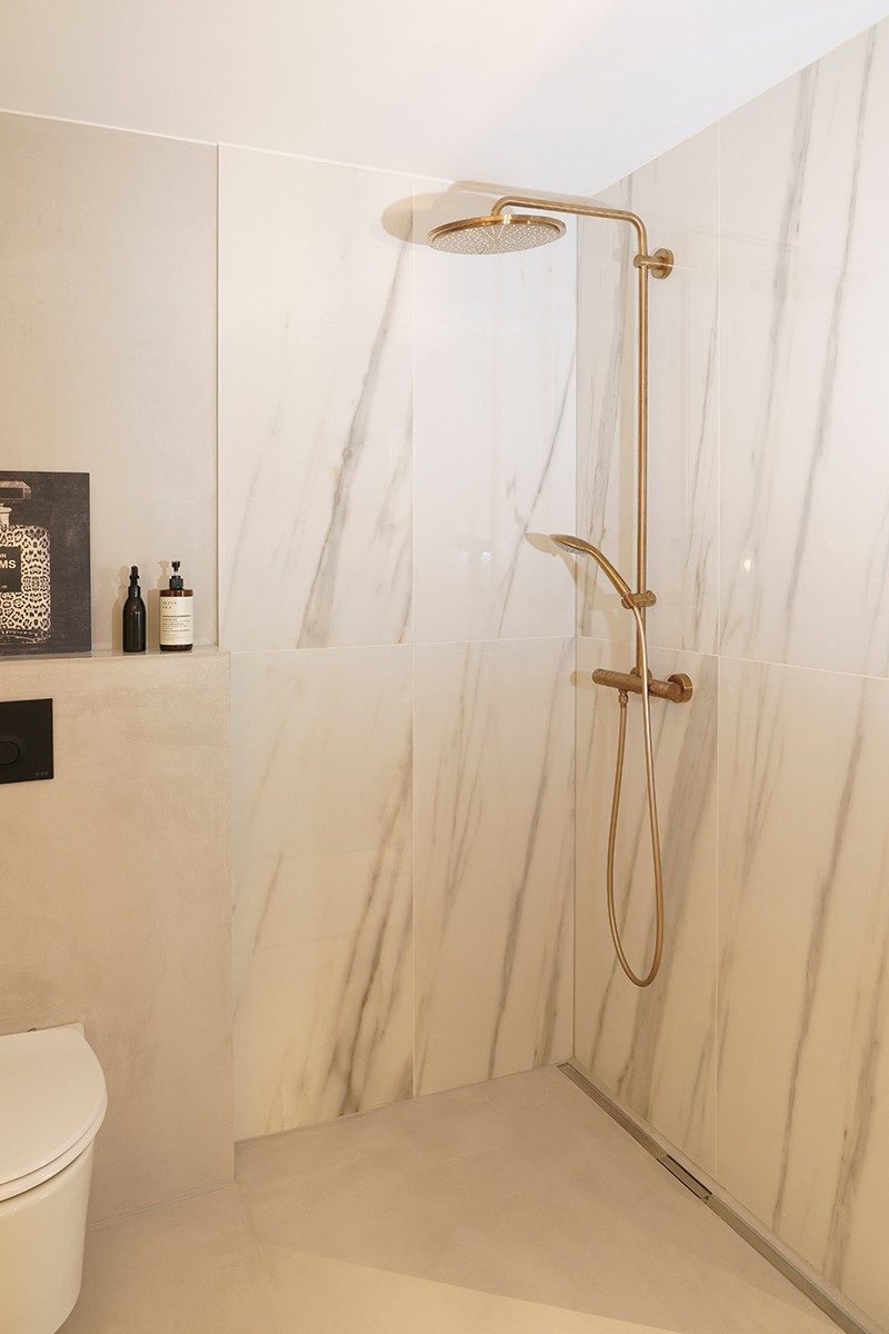 Eine Dusche mit Marmorplatten und goldenen Armatur-Elementen