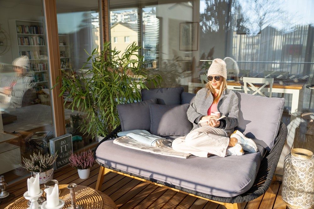 Eine Frau sitzt auf einem Outdoor-Sofa auf einer Loggia.