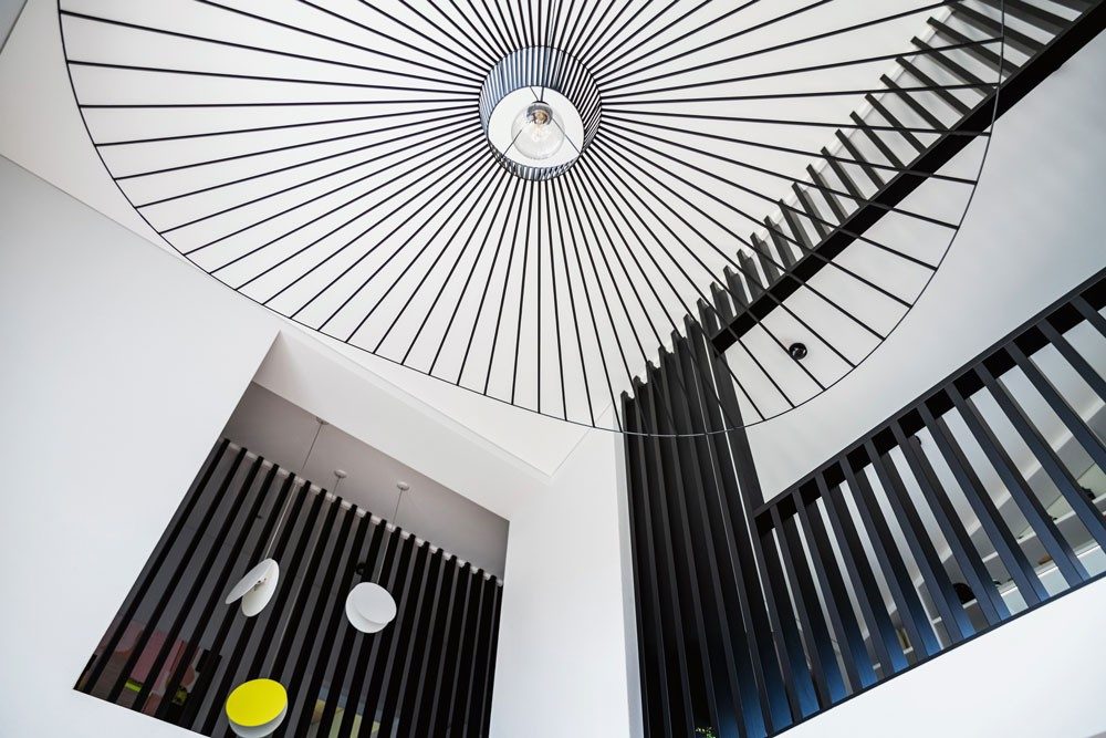 Eine grosse Deckenlampe mit filigranen, schwarzen Elementen fügt sich perfekt in ein Treppenhaus mit Strebengeländer ein.