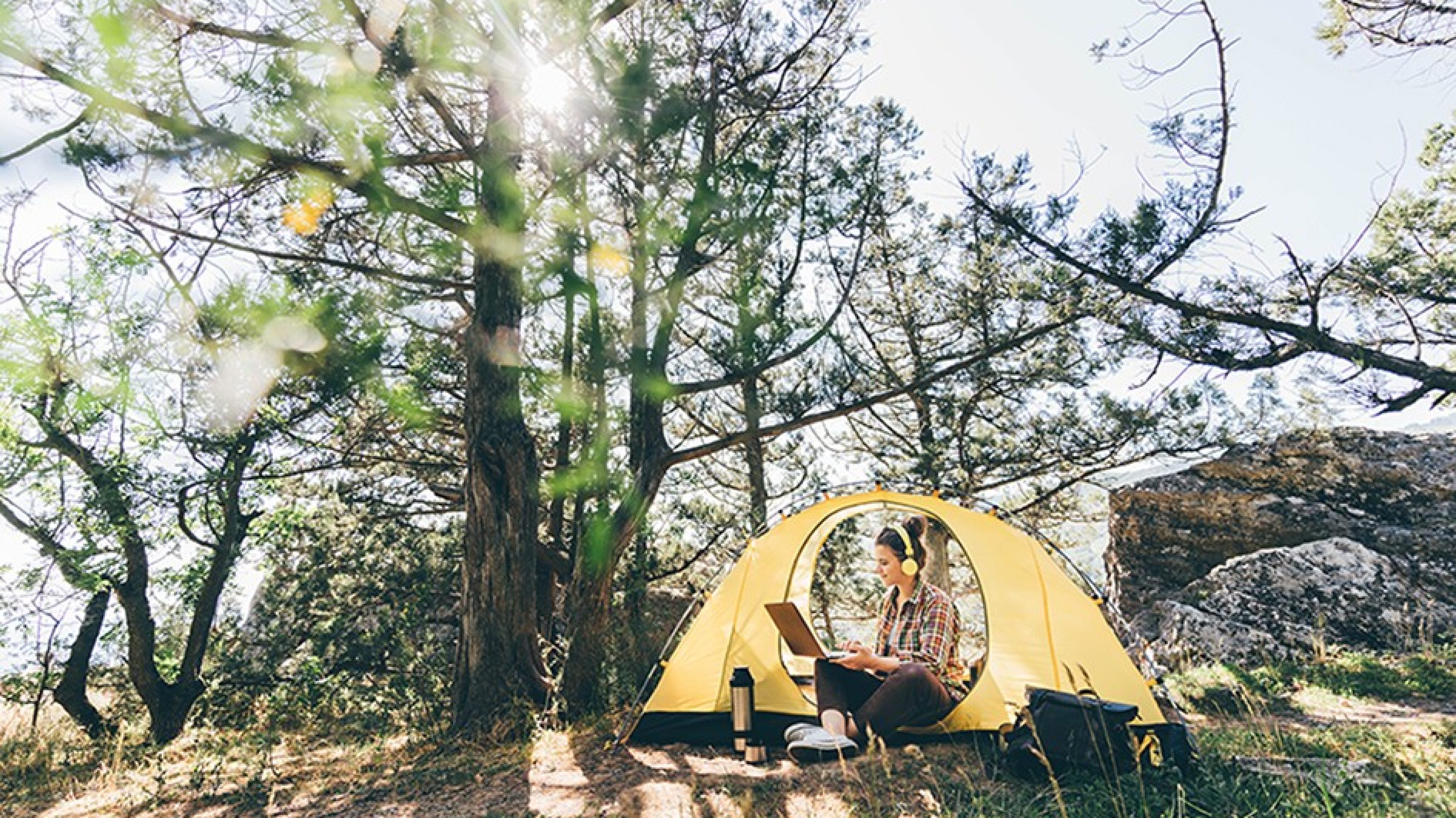 Woman working on laptop in tent in forest. 