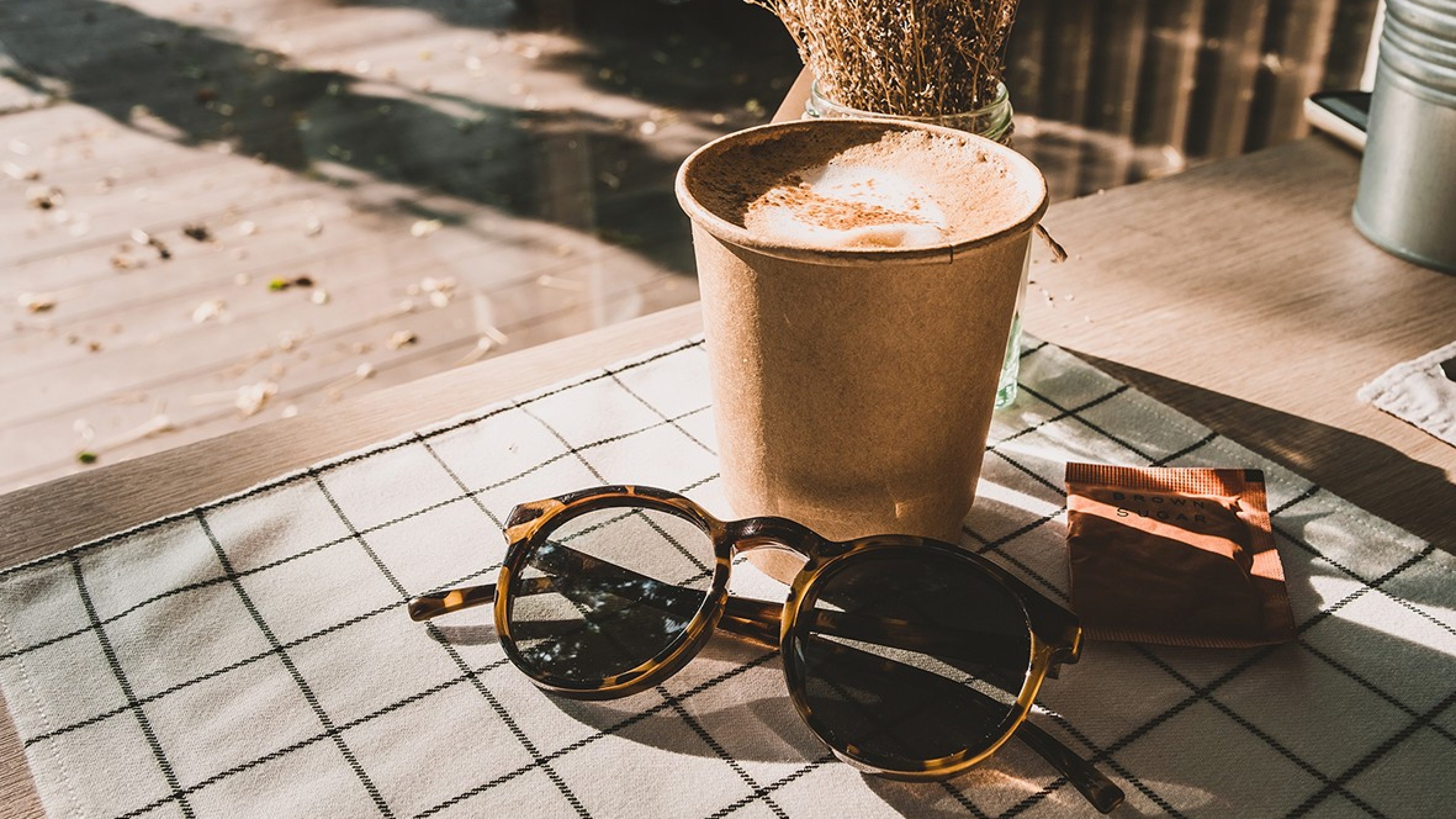 Sonnenbrille liegt neben einem Cappuccino auf dem Tisch. 