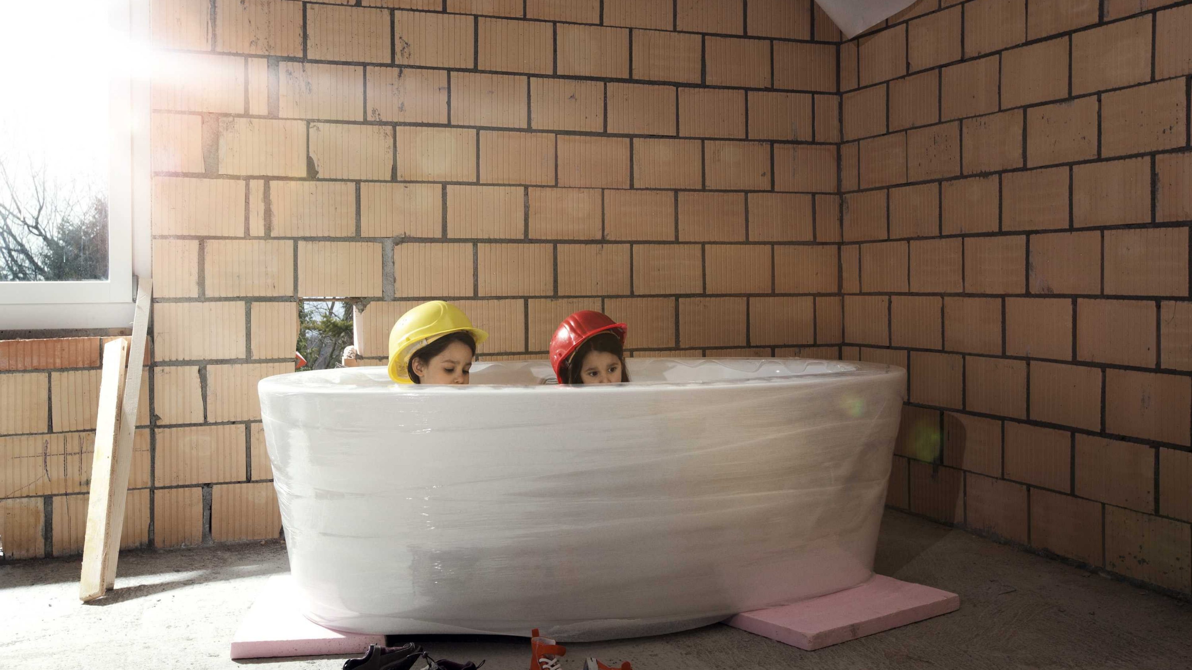 Zwei Kinder sitzen in einer Badewanne im Rohbau des Eigenheims.