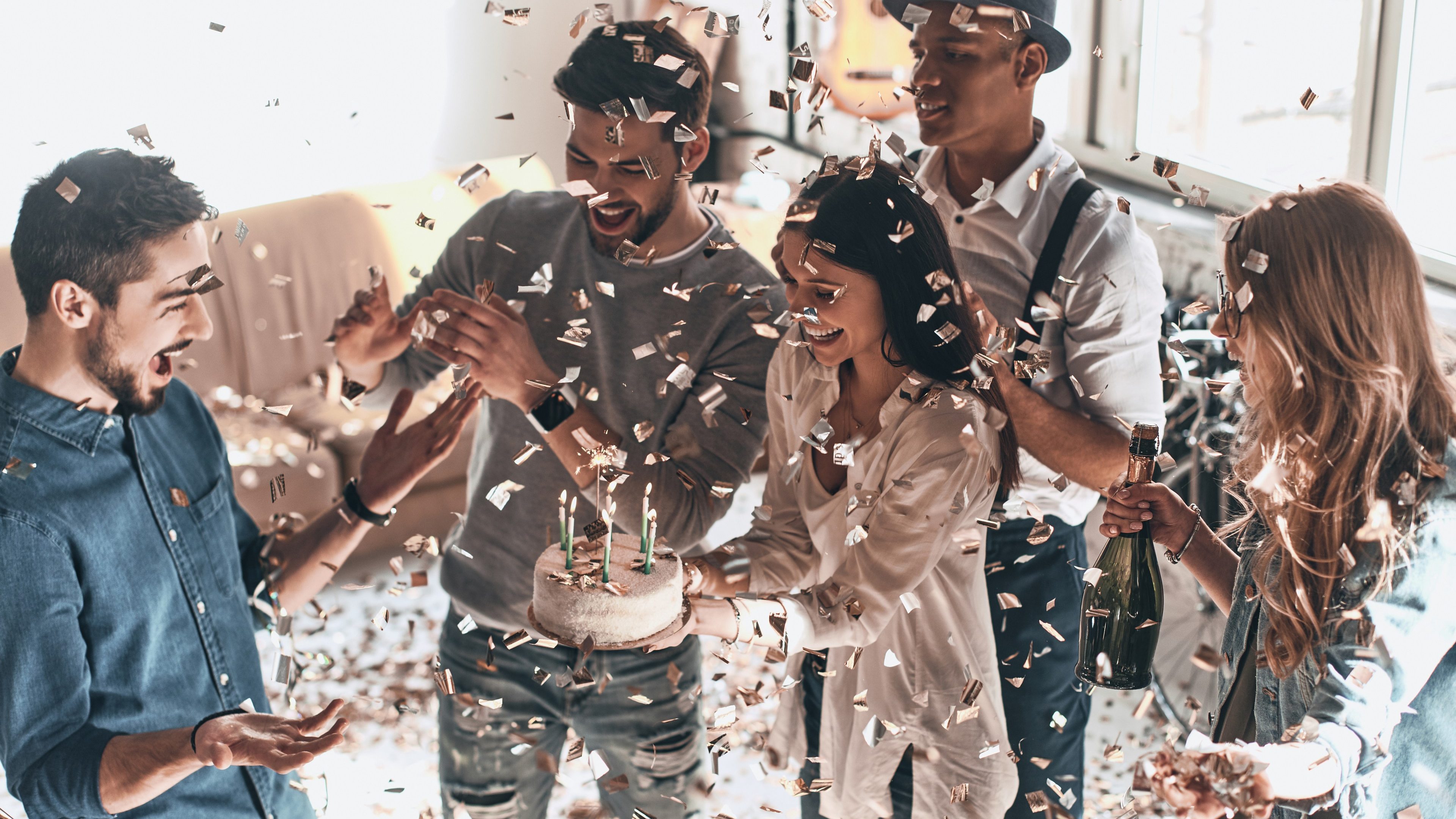 Happy birthday! Top view of happy young man celebrating birthday among friends while standing in room with confetti flying around