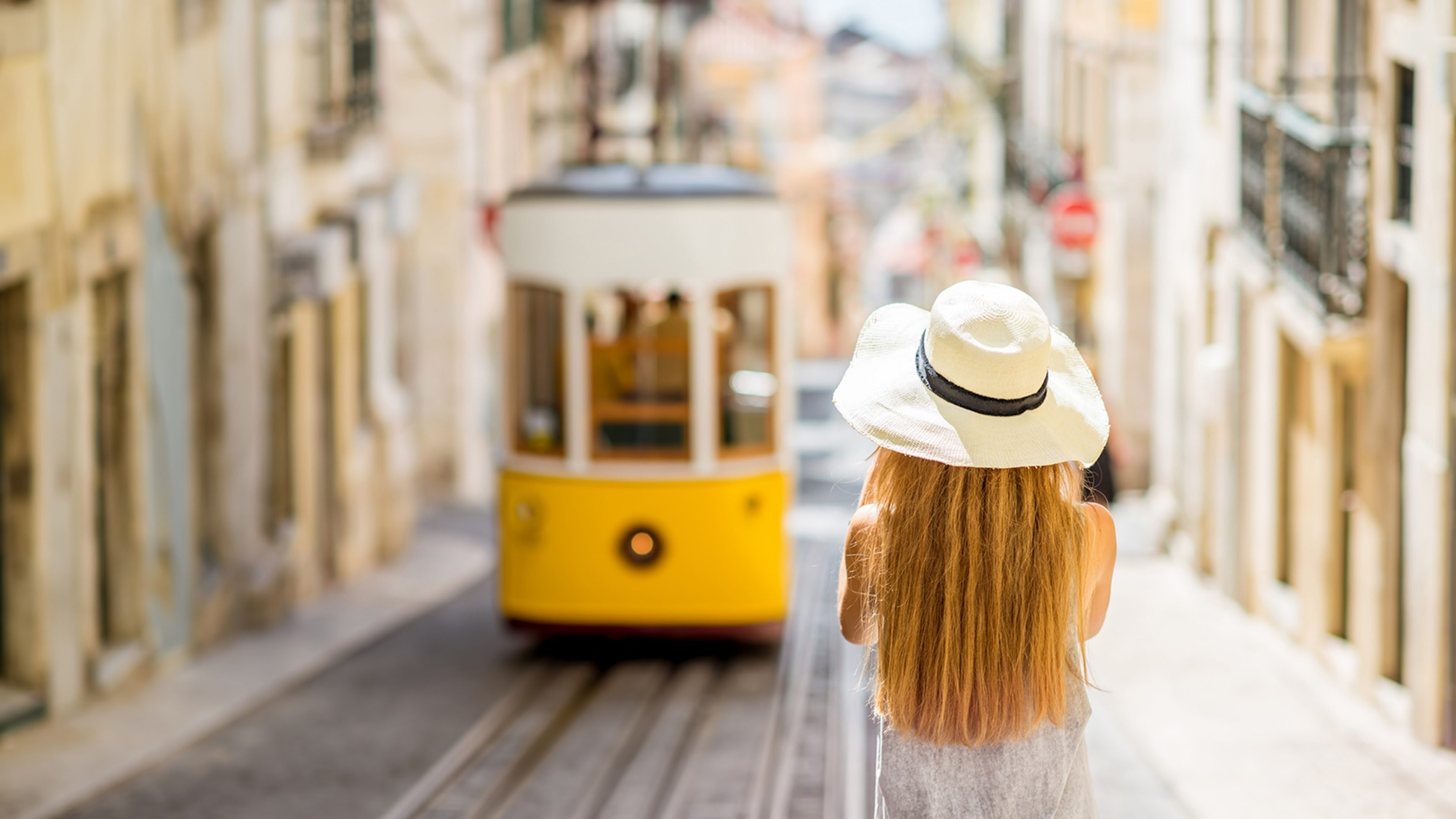 Young woman tourist photographing famous retro yellow tram on the street in Lisbon city, Portugal