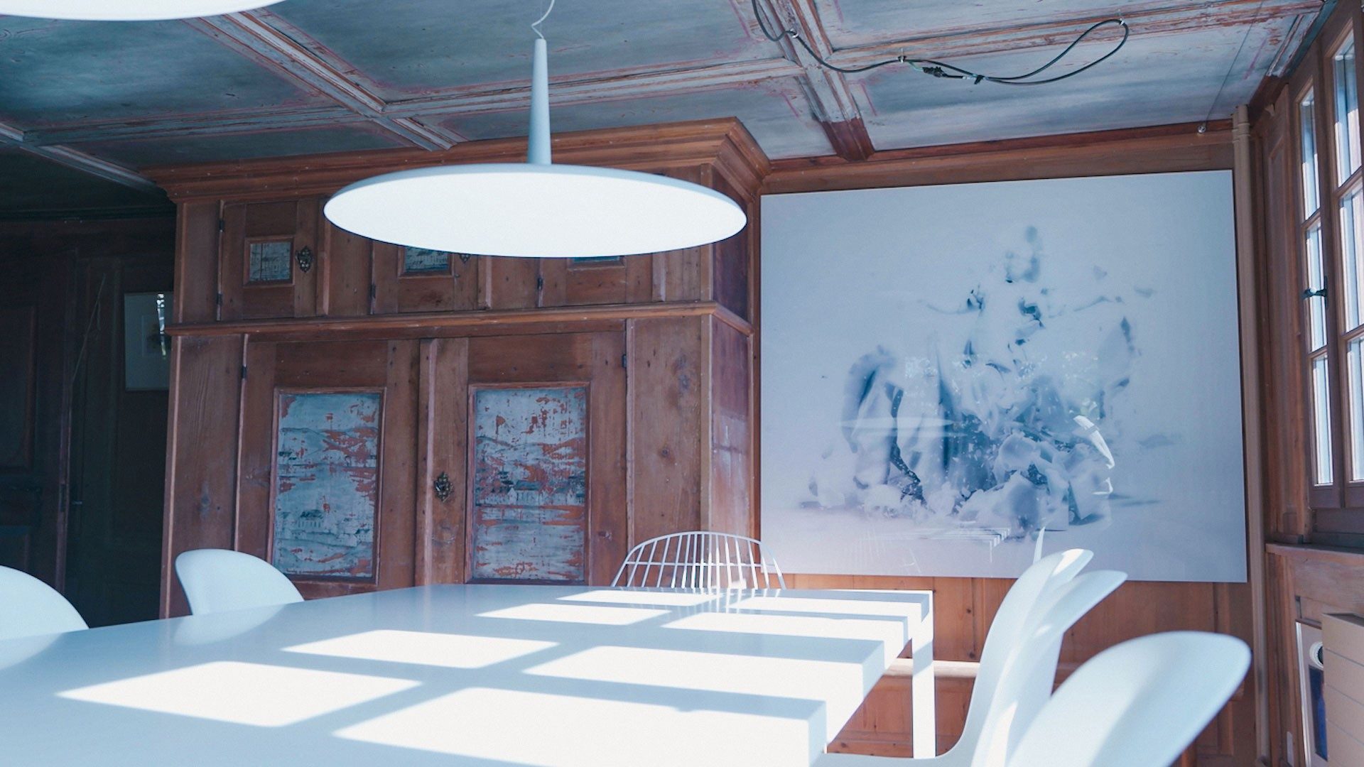 Une table blanche dans une pièce lambrissée, avec des murs arborant des œuvres modernes.