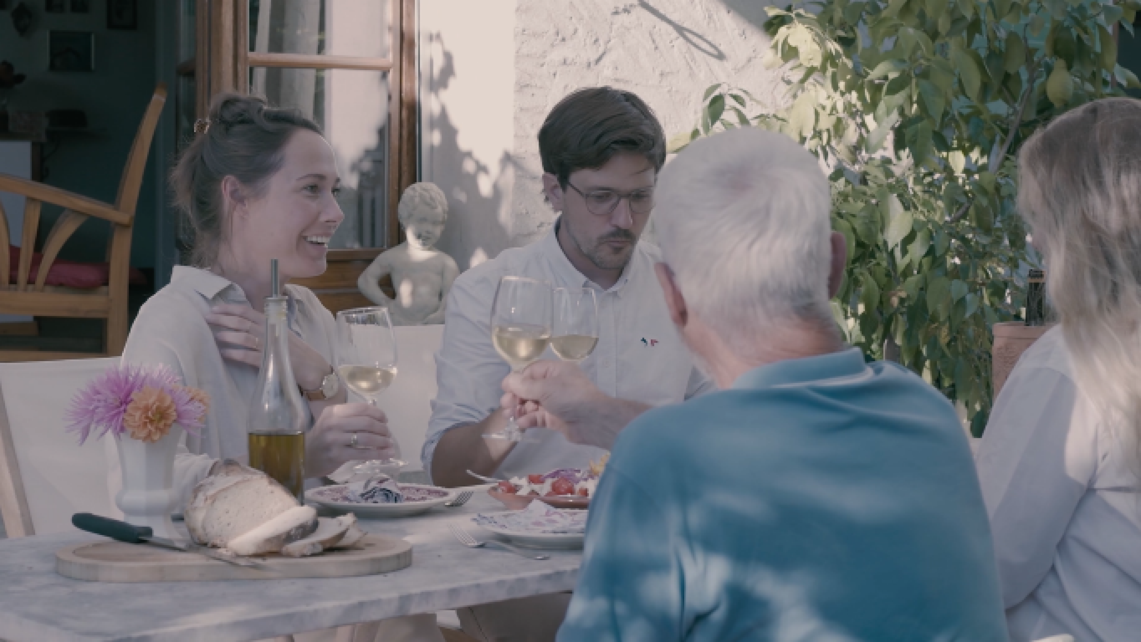 Quatre personnes trinquent sur la terrasse, un verre de vin à la main. 