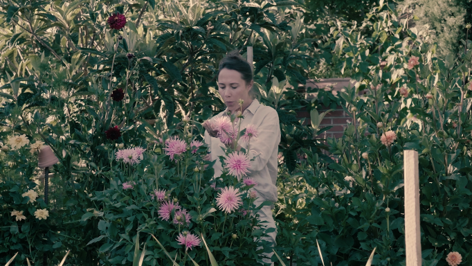 Une femme se tient debout dans un jardin, entourée de plantes. 