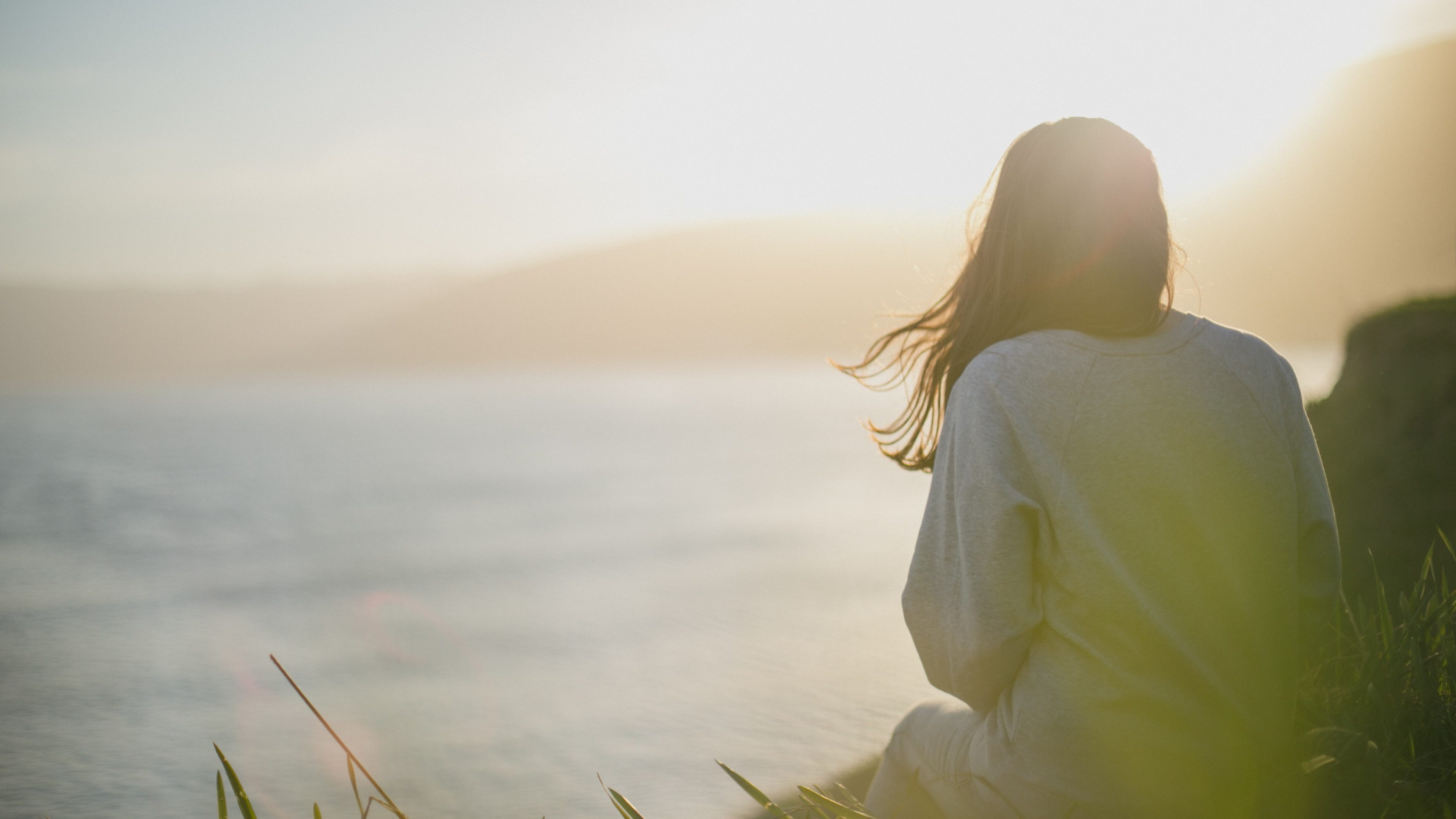 Une femme est assise sur la côte et regarde la mer.