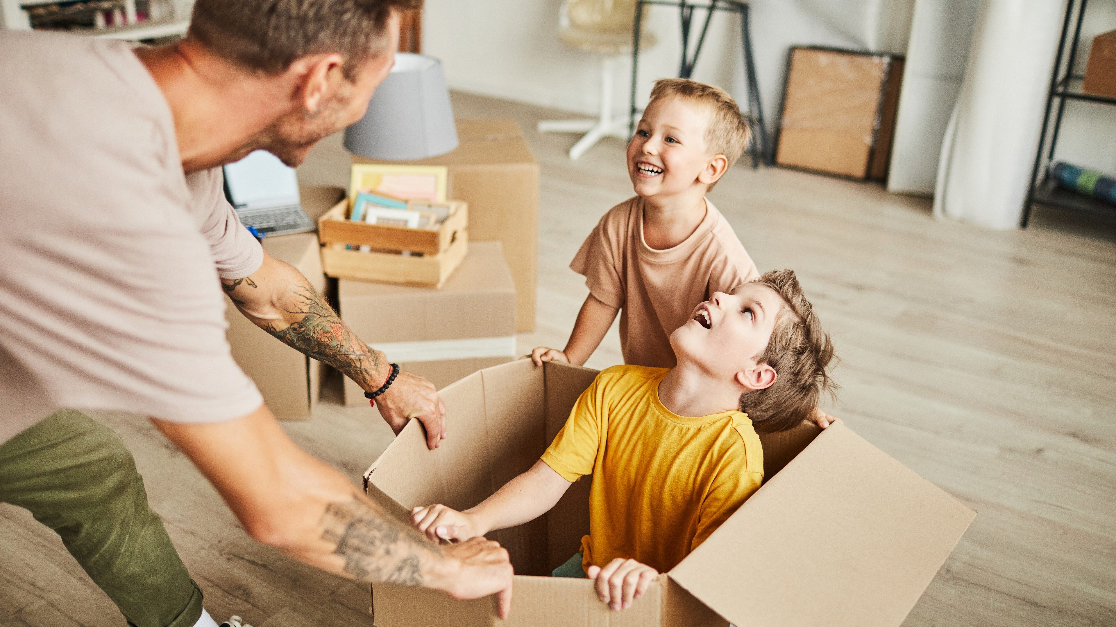 Portrait of happy father playing with two boys in cardboard boxes while family moving to new house, copy space