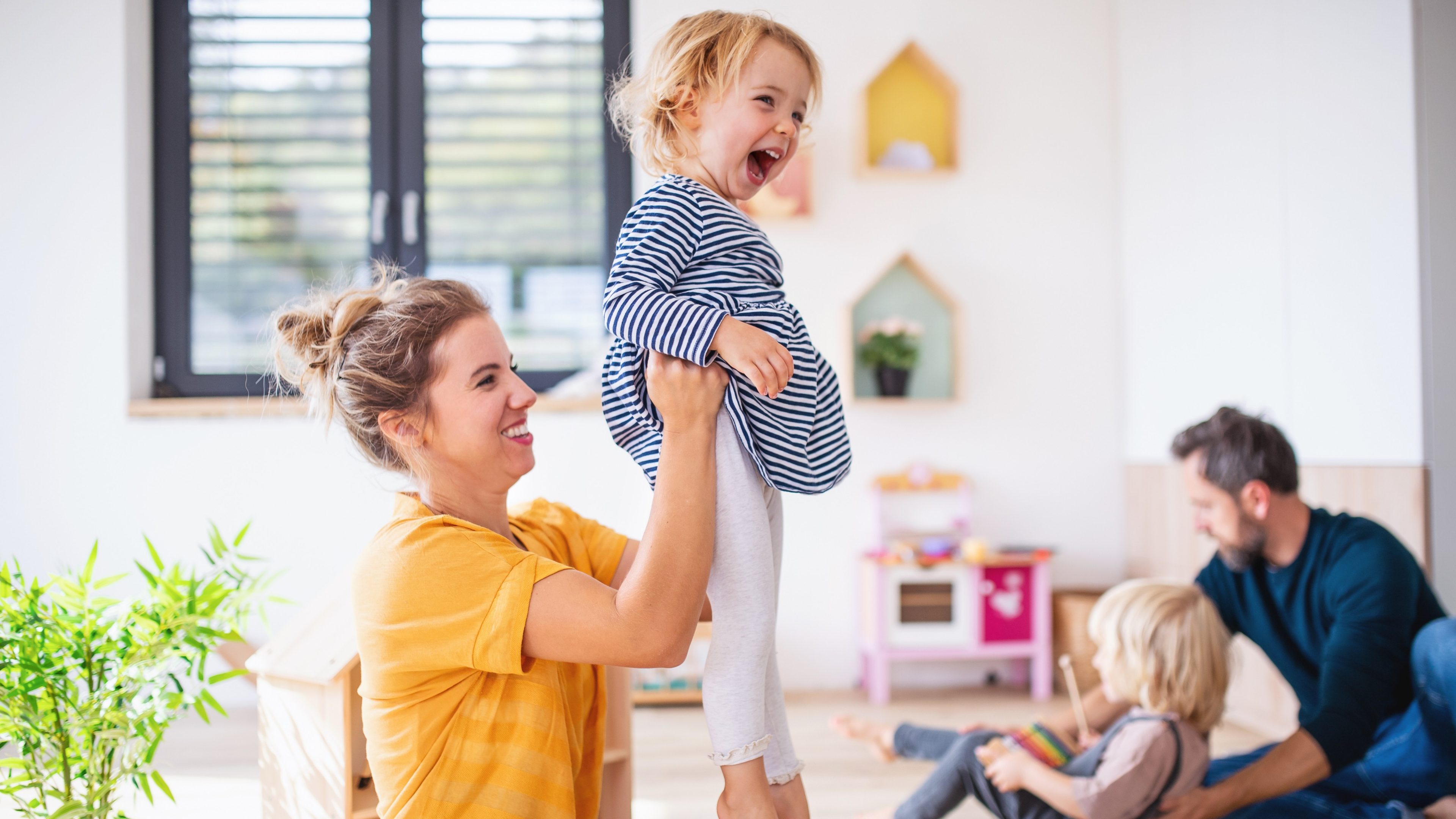 Young family with two small children indoors in bedroom, having fun.