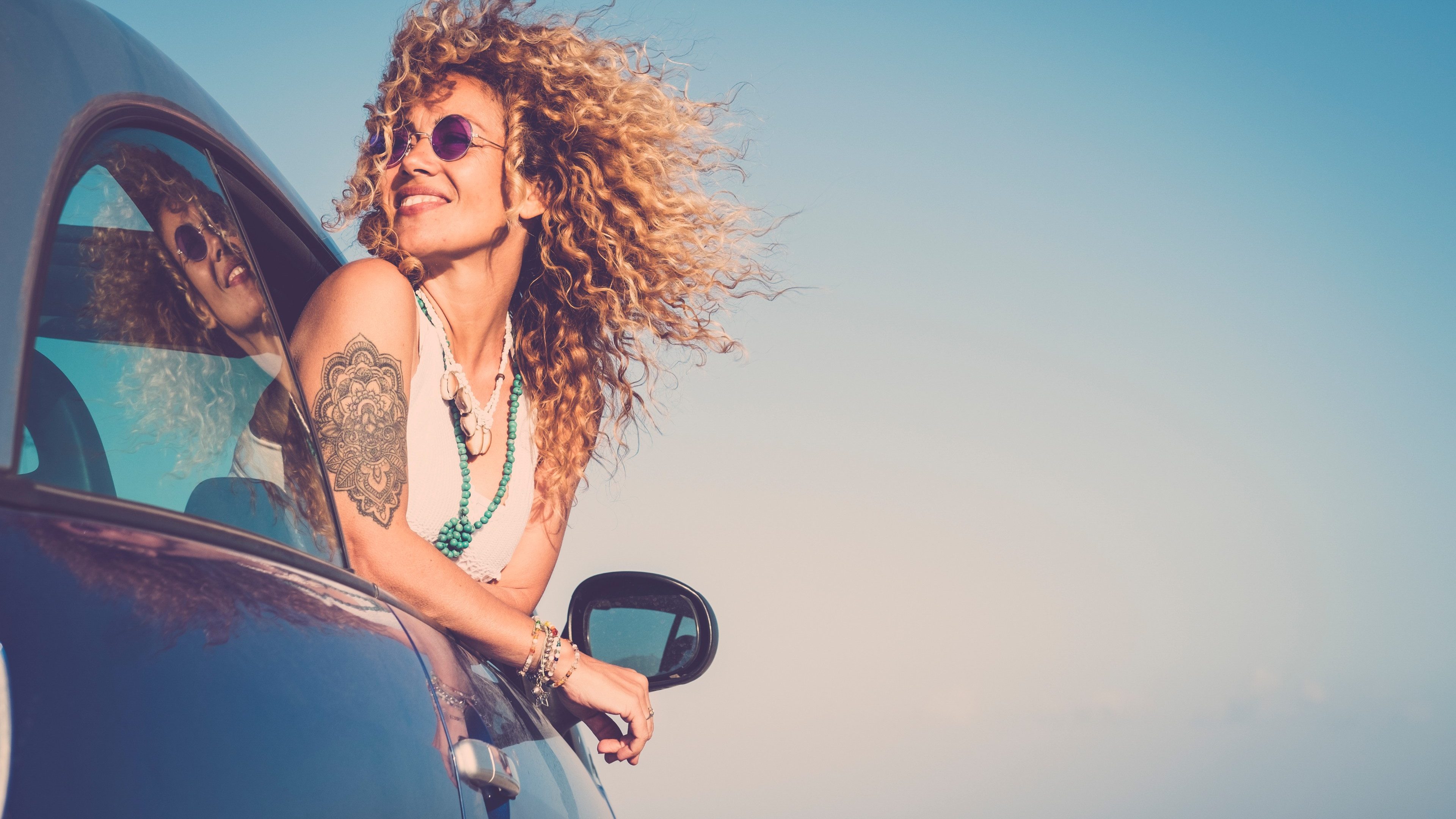 Attractive curly blonde young woman smile and enjoy the wind outside the car - concept of beauty and travel for happy and cheerful caucasian people - alternative lifestyle female feel the freedom and joy