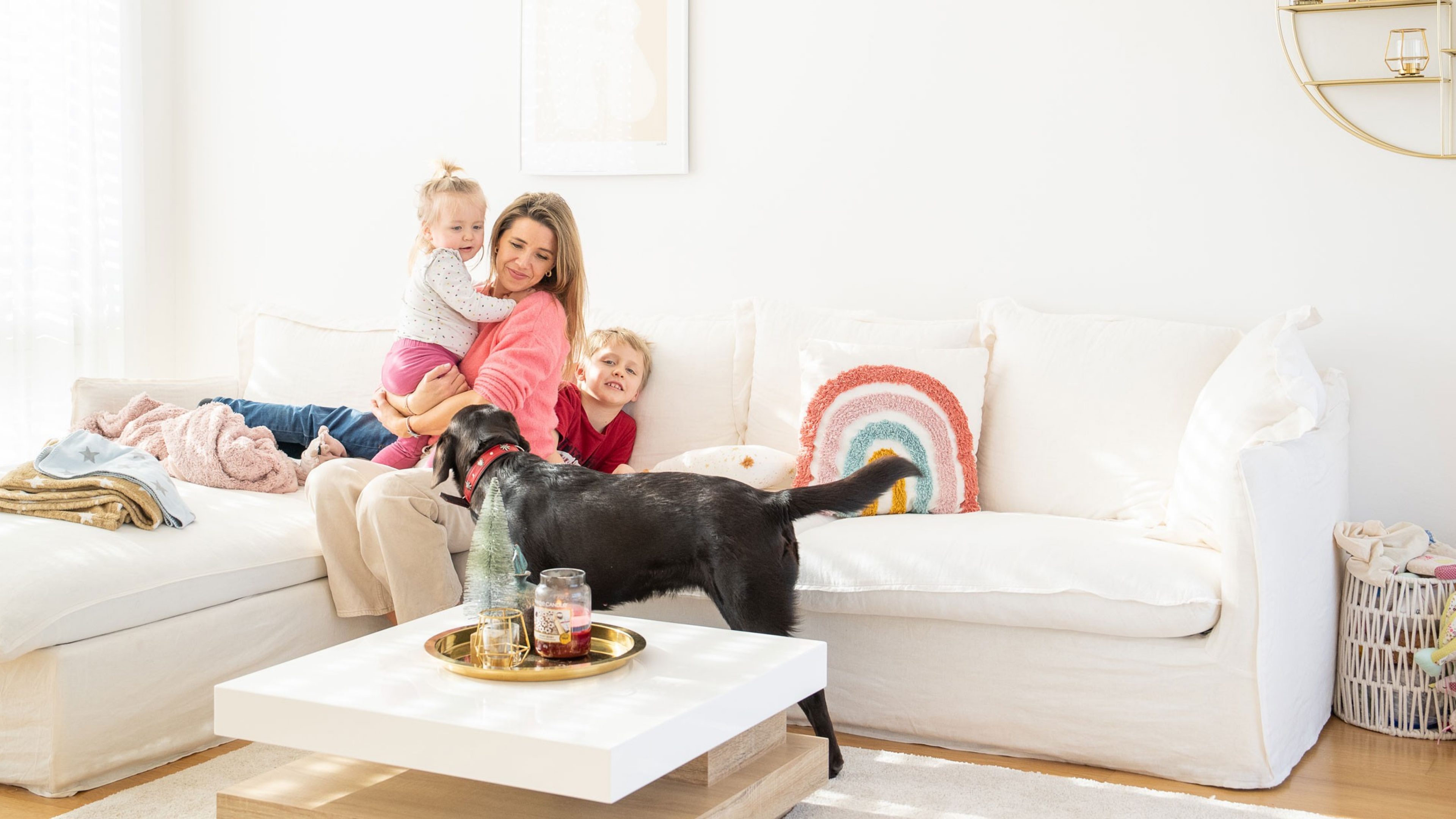 Une femme et deux enfants assis sur le canapé. Devant se tient une chienne Labrador.