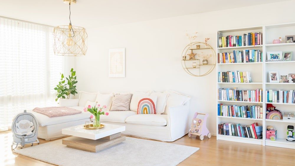Un salon avec un canapé blanc flanqué de jouets; à côté, une étagère avec une multitude de livres. 