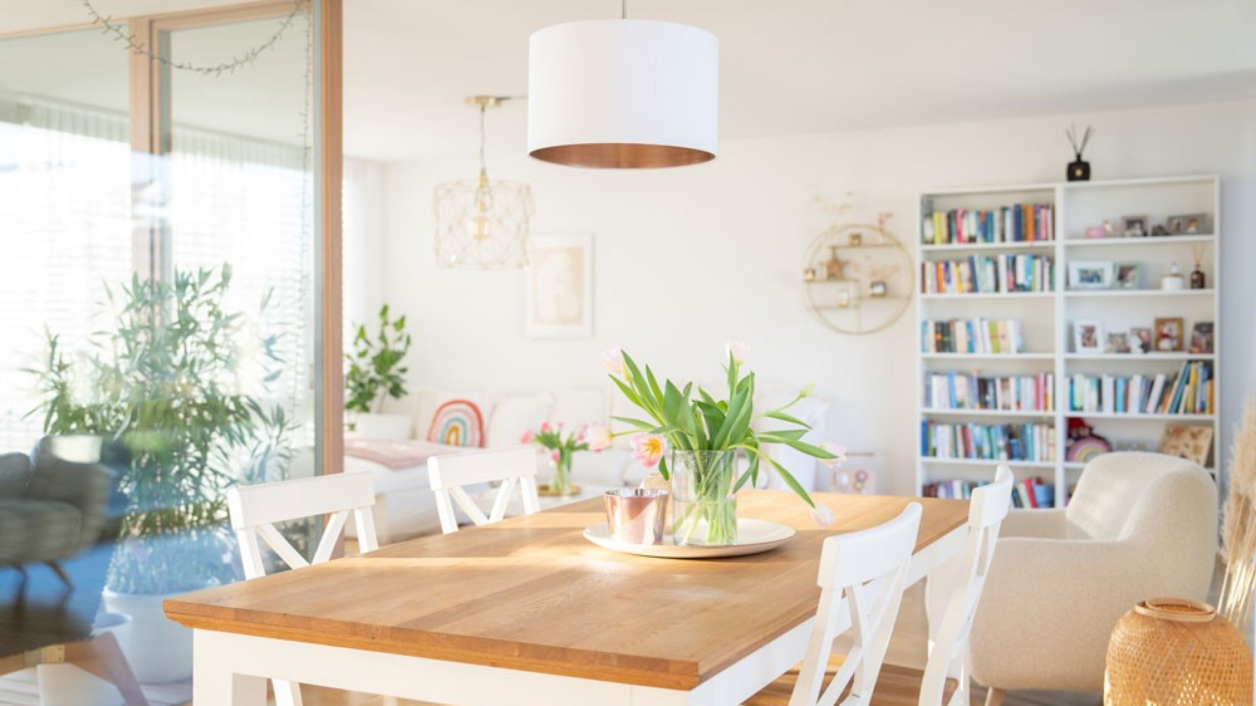 Une table à manger ornée de belles tulipes, devant une loggia et le salon avec une bibliothèque.