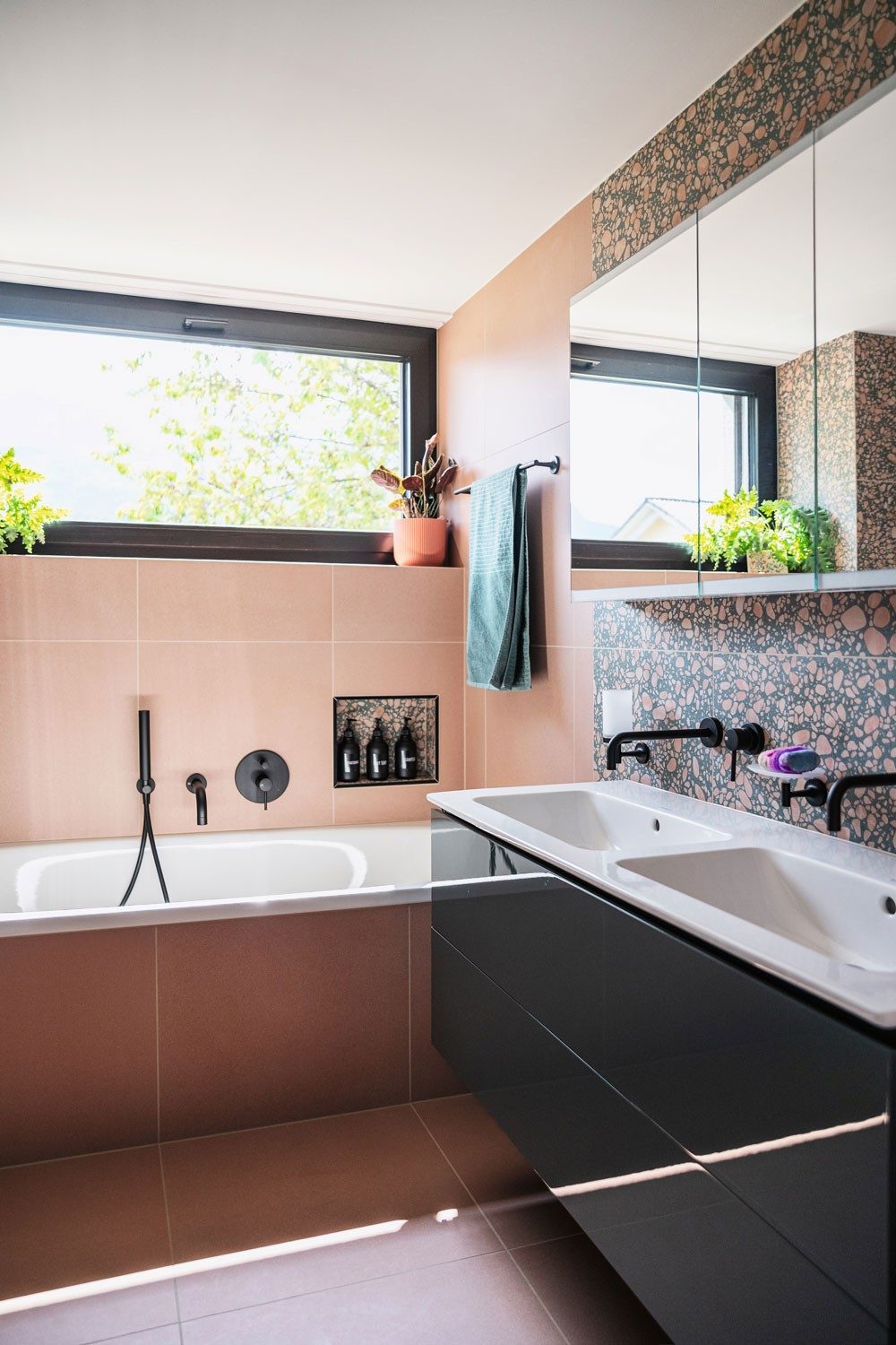 Une salle de bain à la faïence rose et aux meubles de vasques noirs.