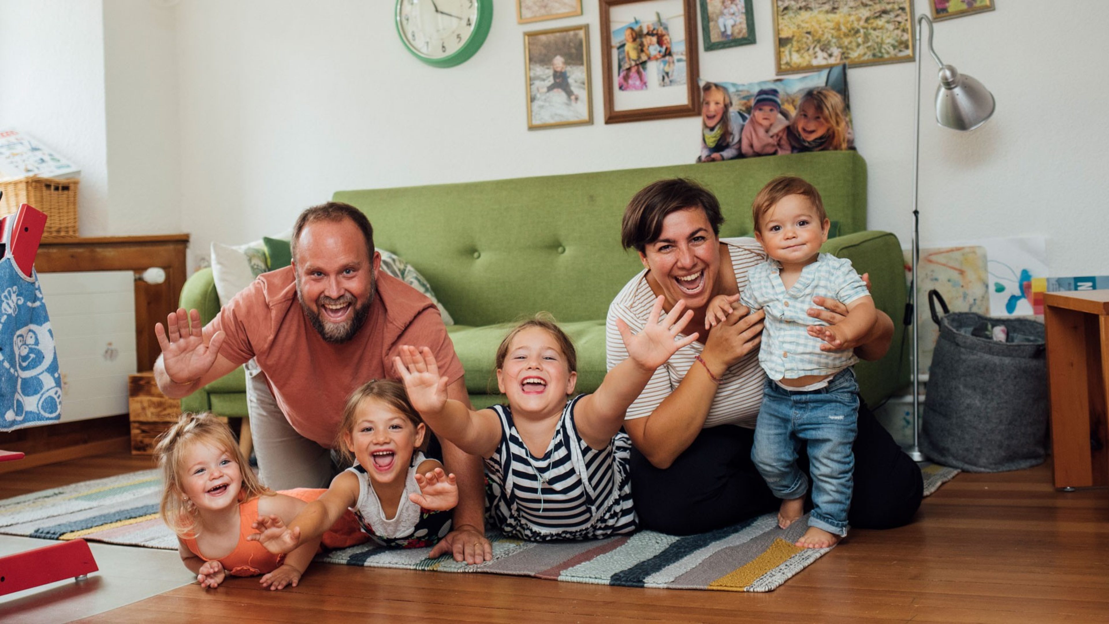 Parents avec enfants riant dans un salon avec un canapé vert et des tableaux accrochés au mur