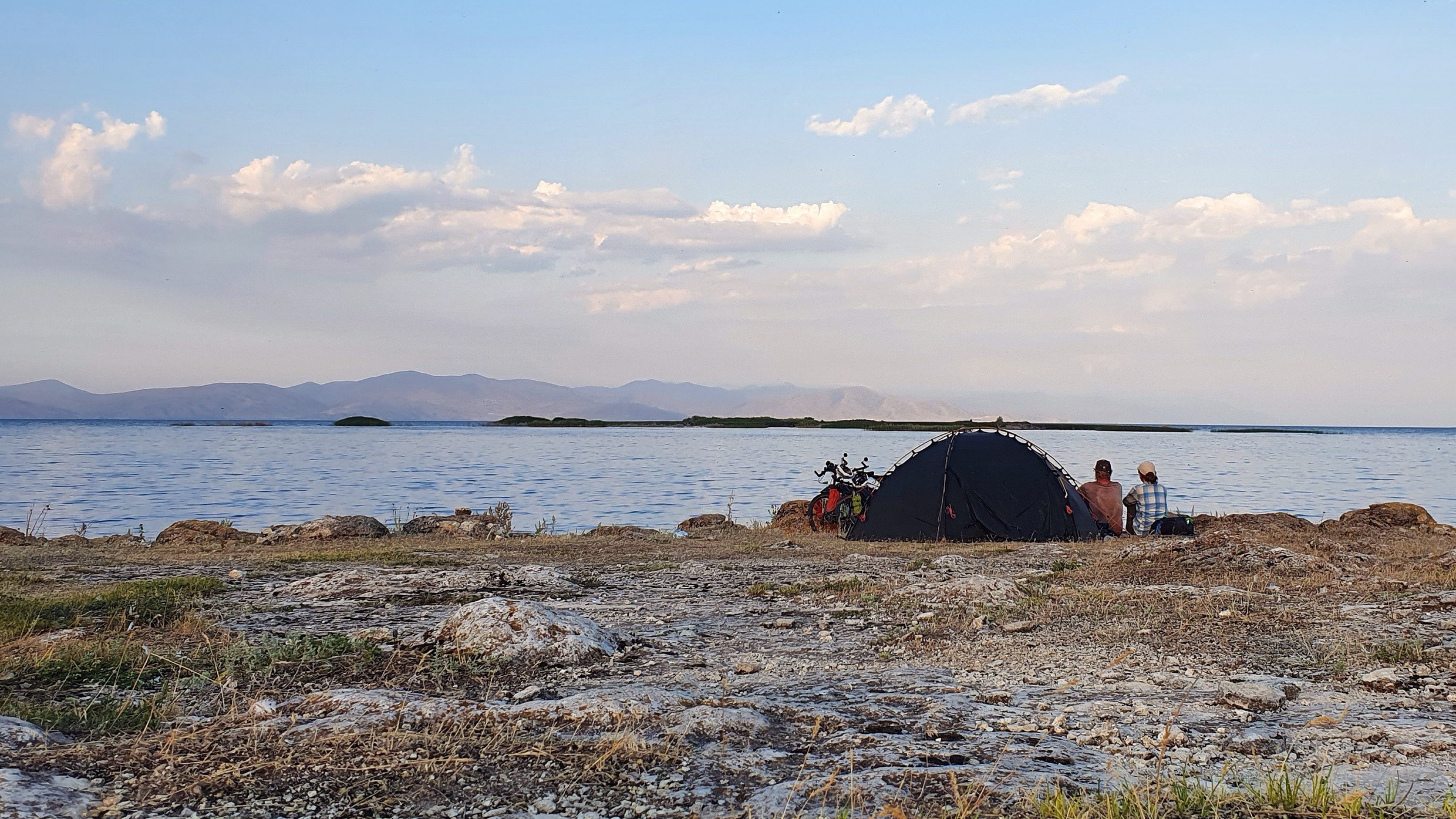 Zwei Abenteurer auf Fahrrädern haben ihr Zelt am See aufgeschlagen und genießen die herrliche Kulisse. Für sie ist die Welt ihr Zuhause und das Leben eine Reise voller Abenteuer und Entdeckungen.