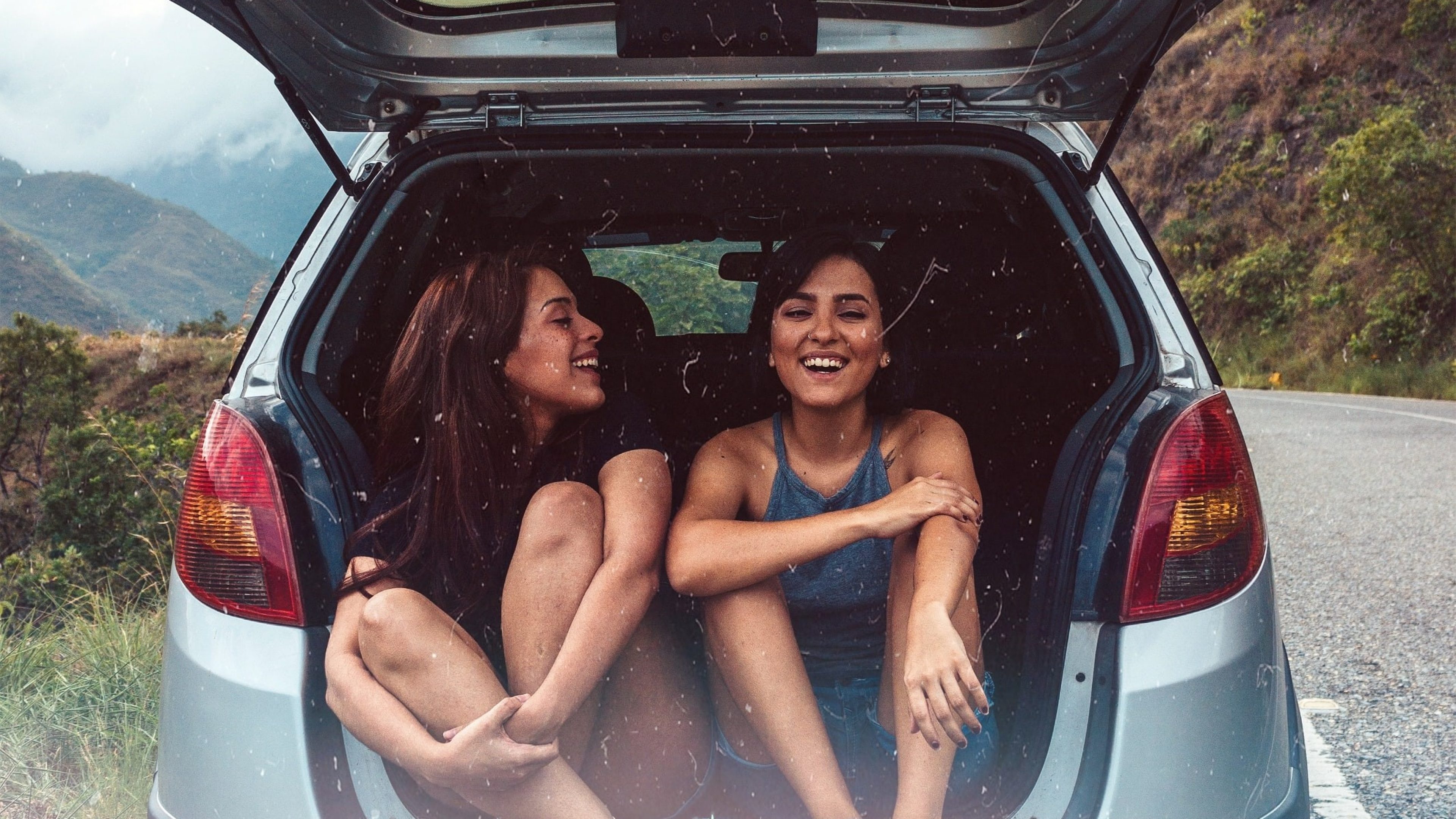 Deux jeunes femmes sont assises dans le coffre ouvert d'une voiture.