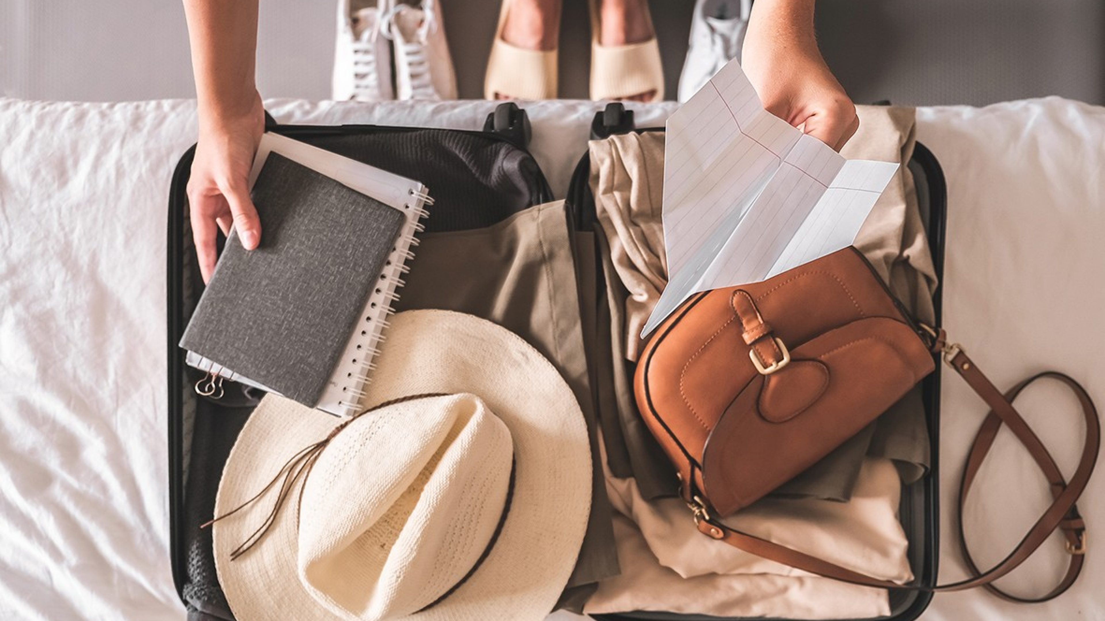 Une femme prépare sa valise, qui est ouverte sur le lit.