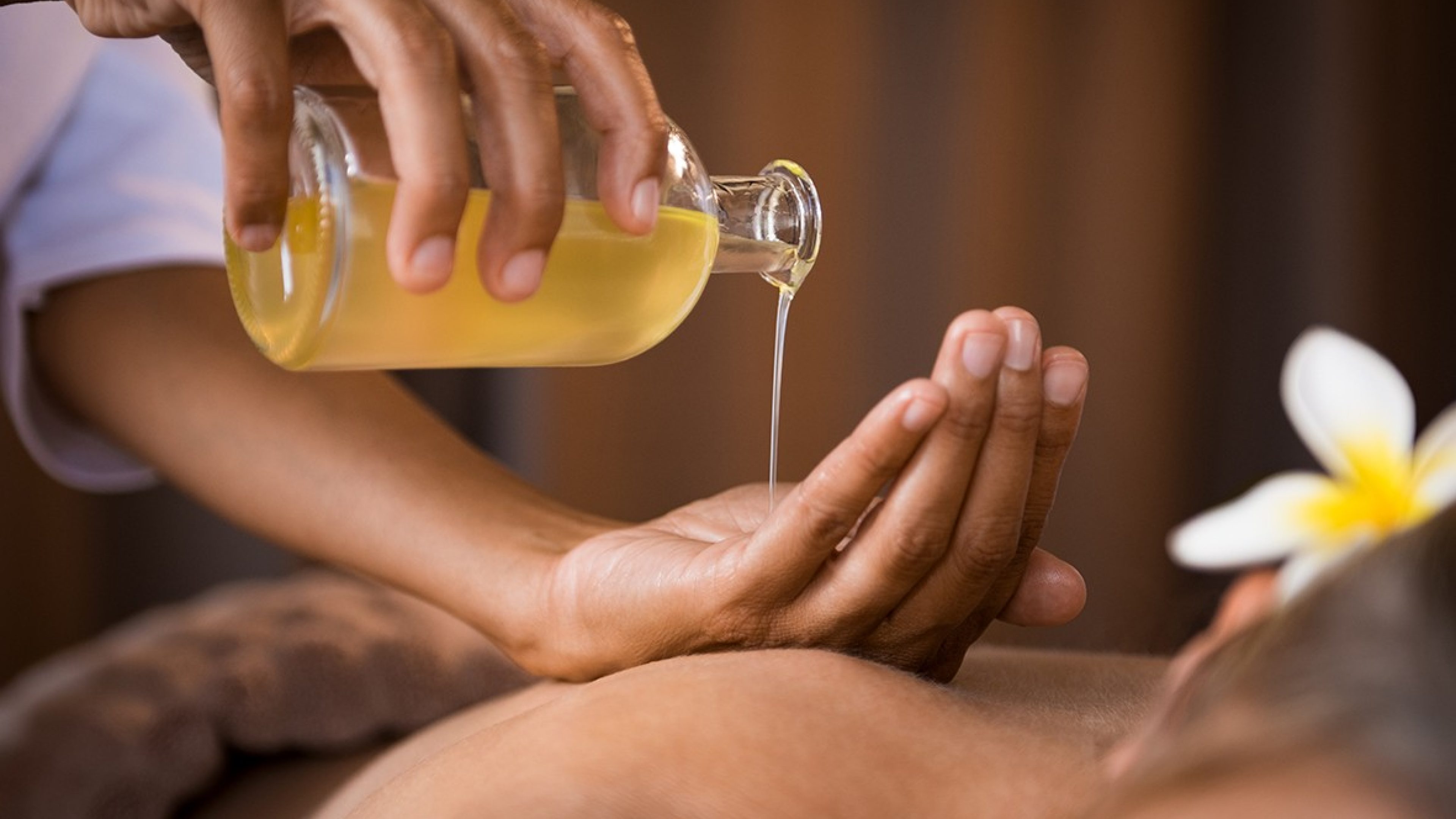 Une masseuse verse de l'huile de massage dans sa main, qui est posée sur le dos d'une femme.