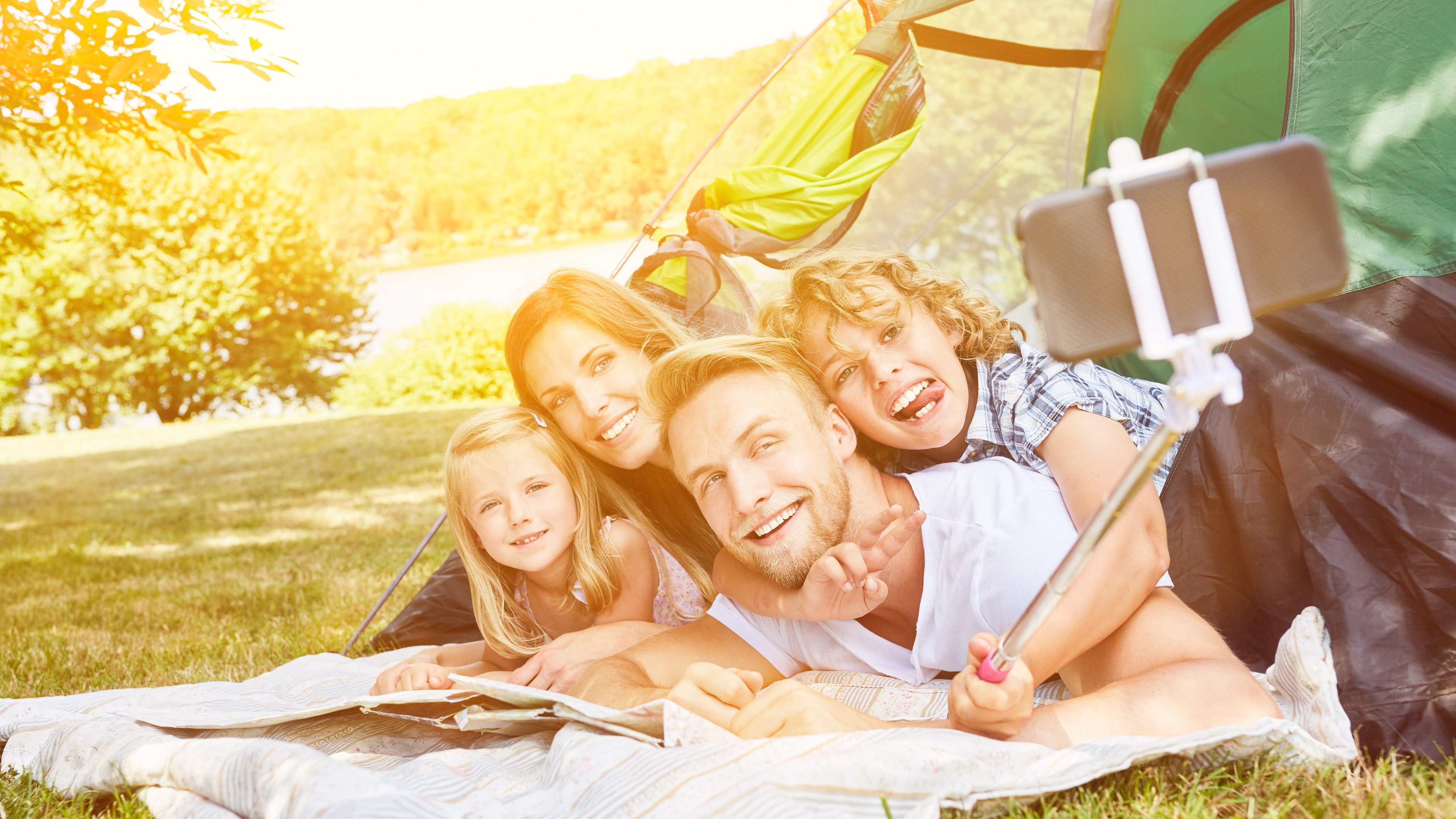 Happy family is making selfie with selfie stick while camping in summer