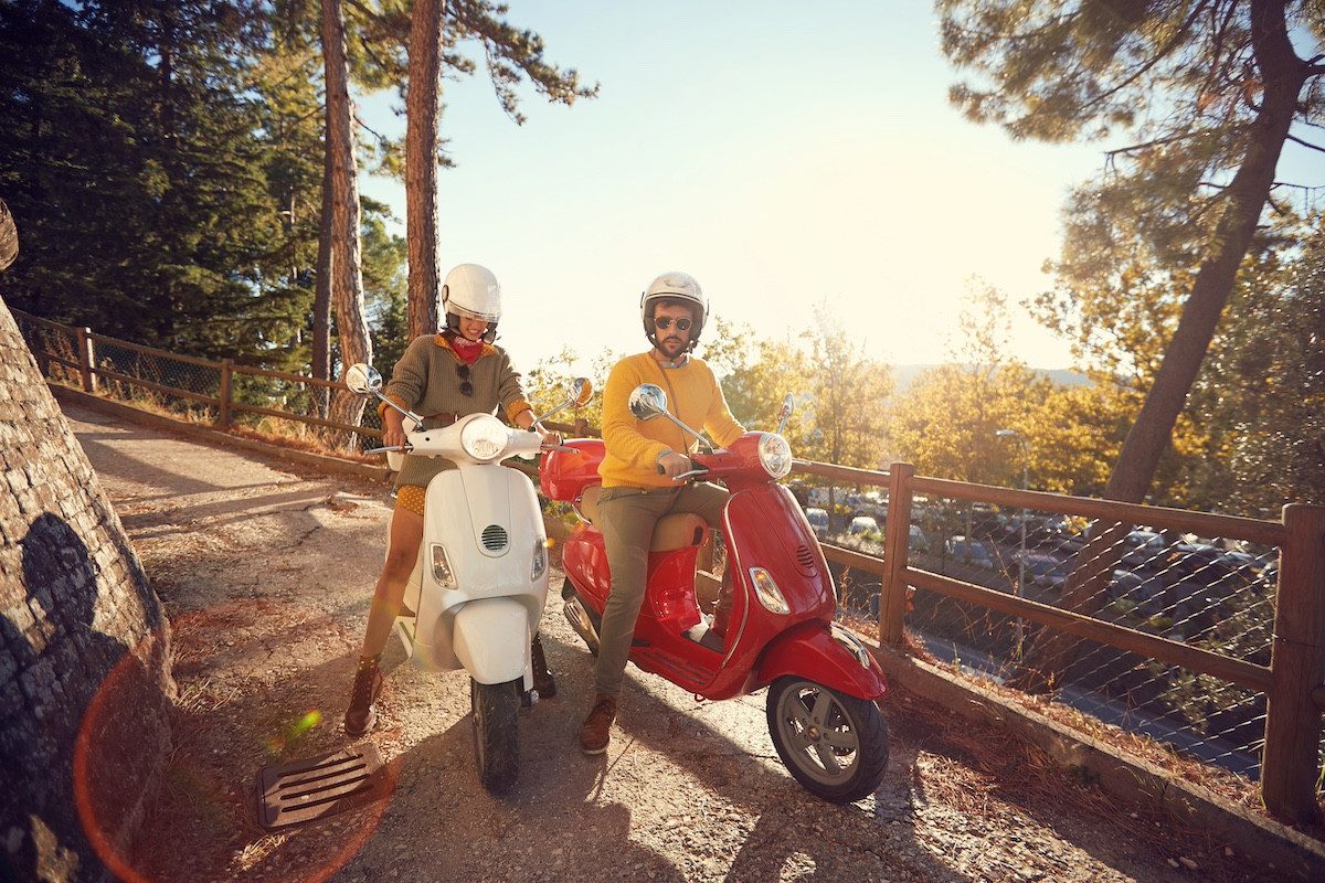 Smiling man and woman riding a scooter and having fun on journey.