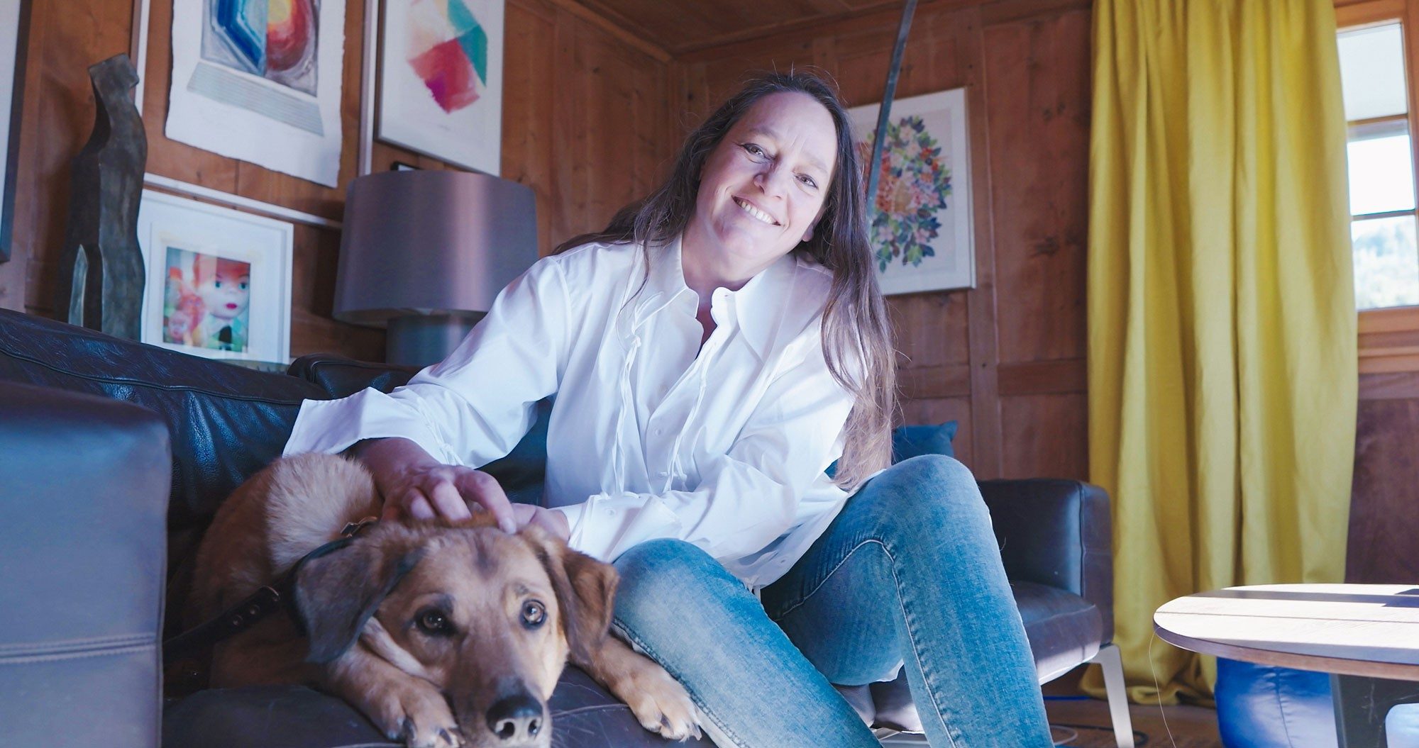 Una donna è seduta su un divano e accarezza un cane. 