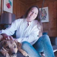 Una donna è seduta su un divano e accarezza un cane. 