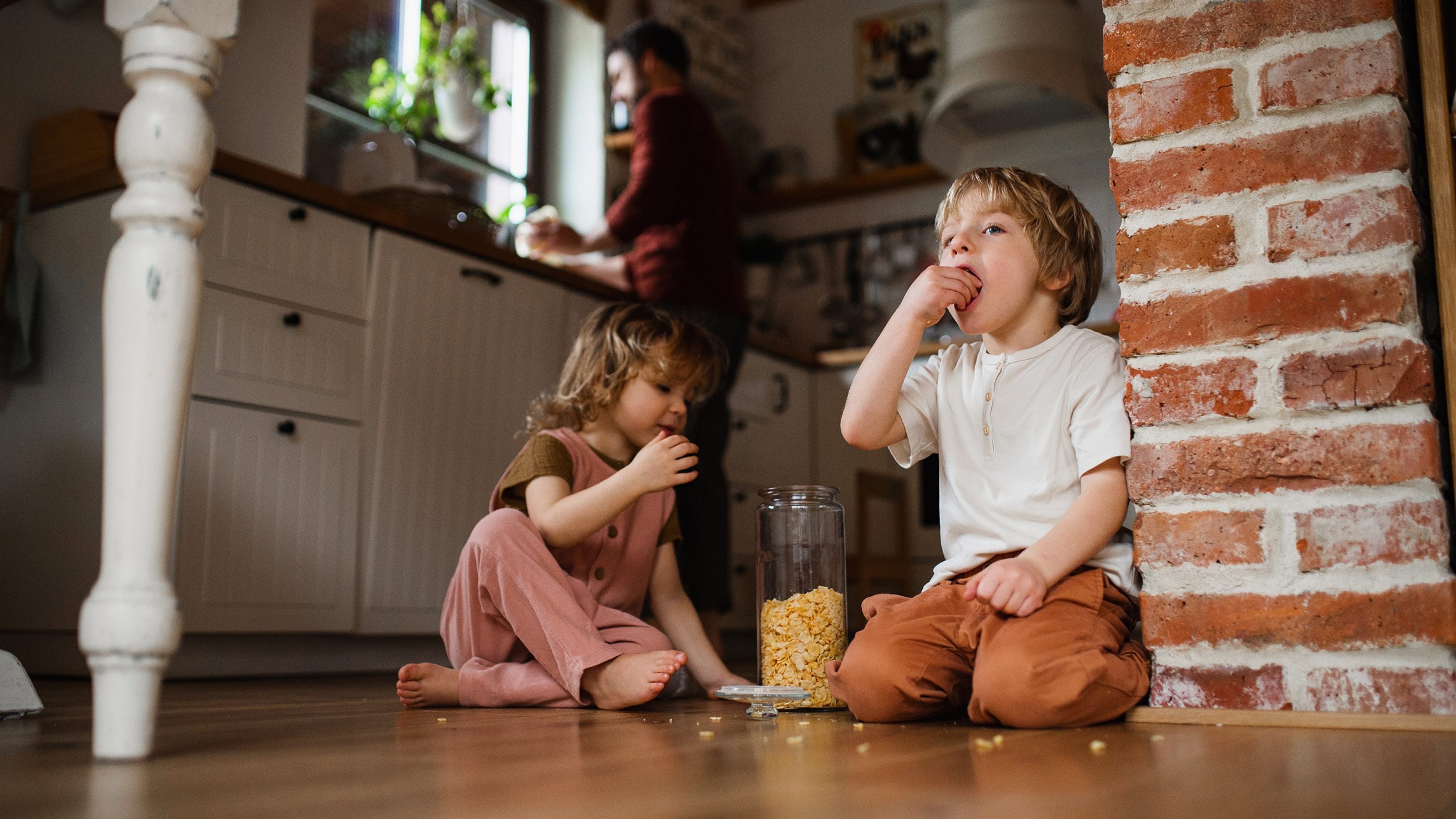Two happy small children with father indoors at home, eating cornflakes on floor.