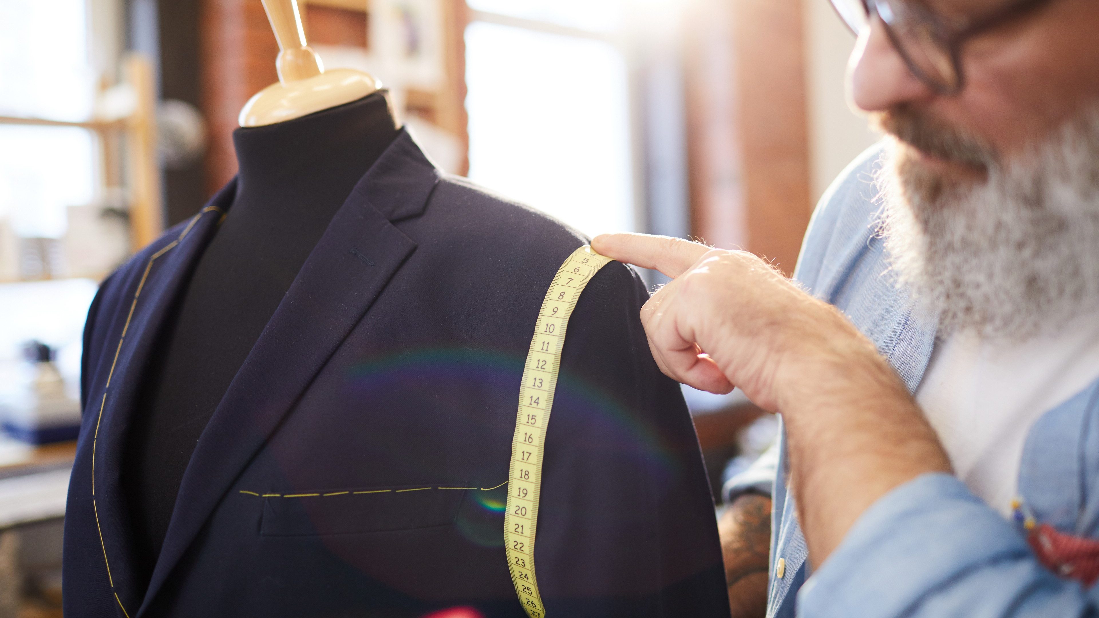Mature tailor measuring girth of jacket sleeve on dummy while sewing new suit for one of clients