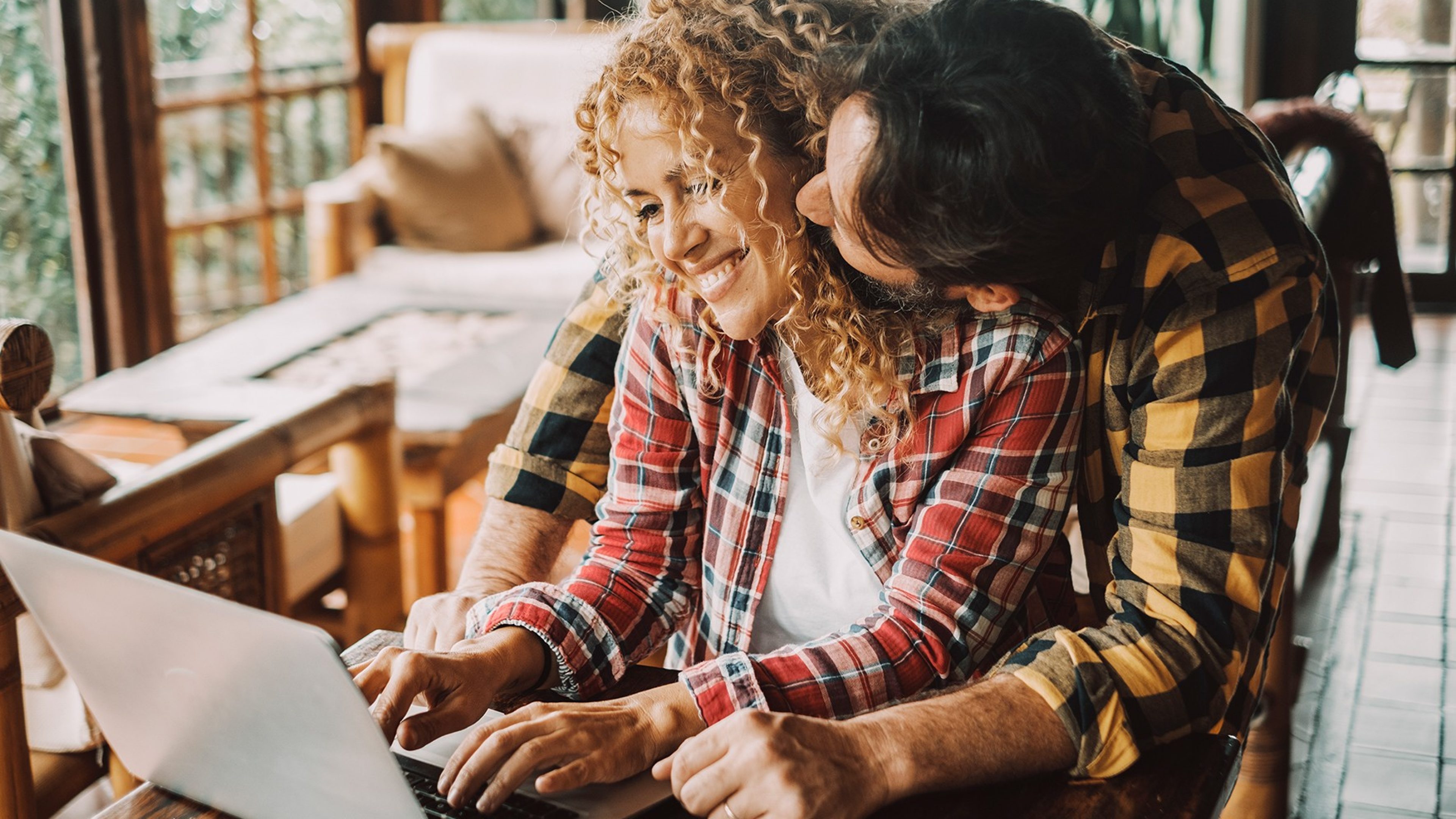 Young adult couple at home have fun and smile while woman work on laptop computer. Concept of modern and happy people couple enjoying love and relationship living together. man hug woman from back