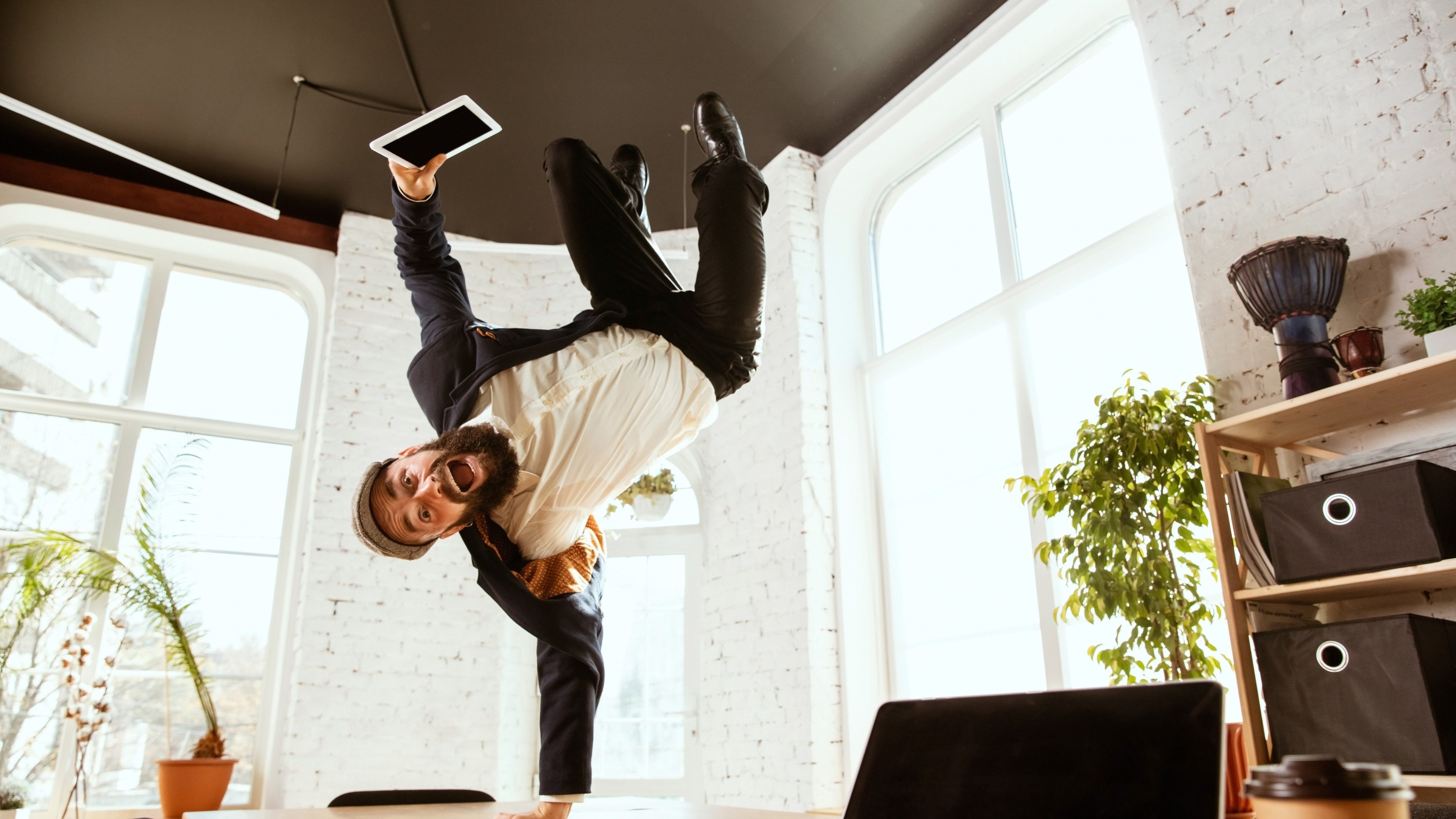 Young caucasian businessman having fun dancing break dance in the modern office at work time with gadgets. Management, freedom, professional occupation, alternative way of working. Loves his job.