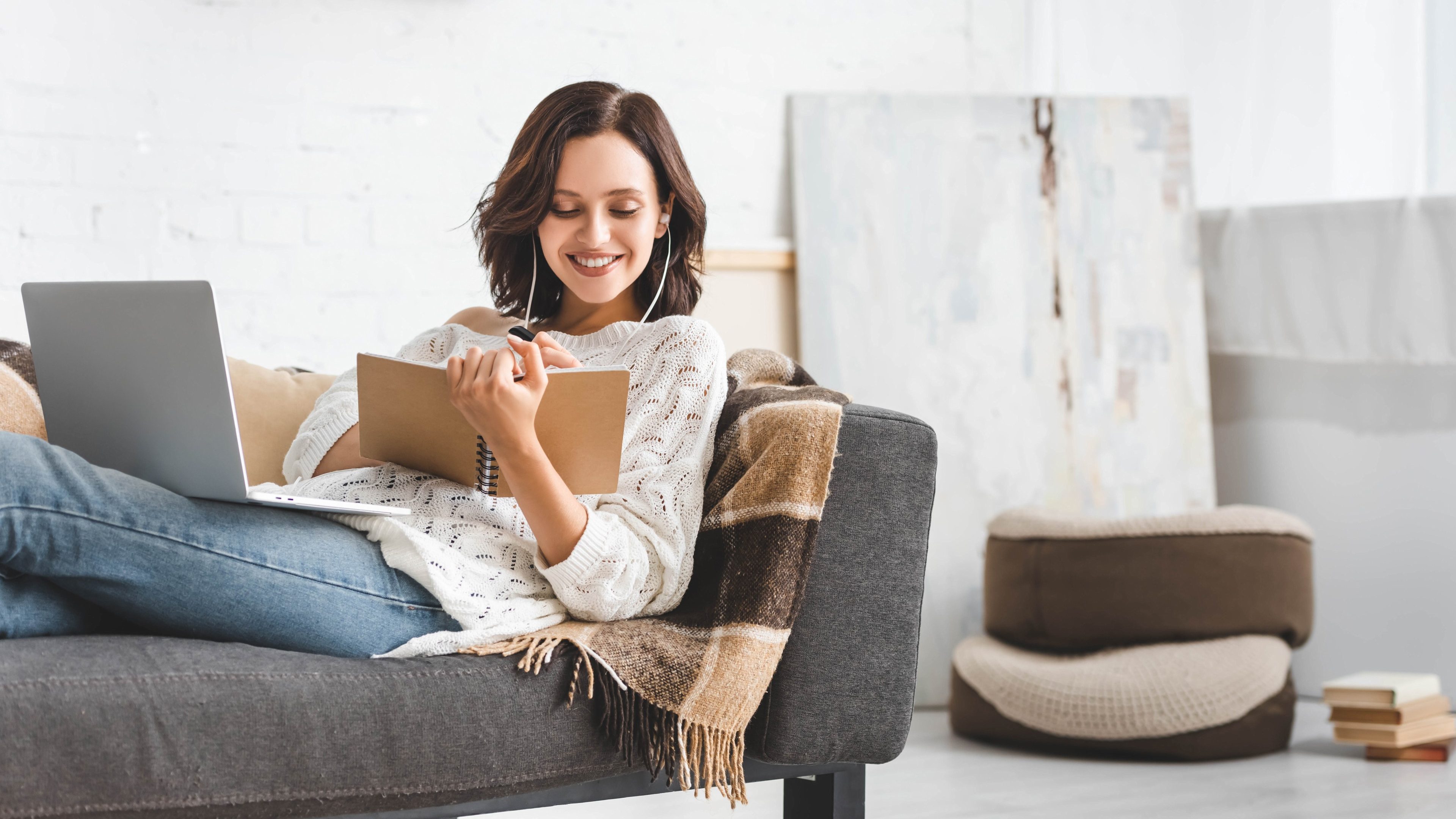 attractive cheerful girl studying online with notepad, earphones and laptop
